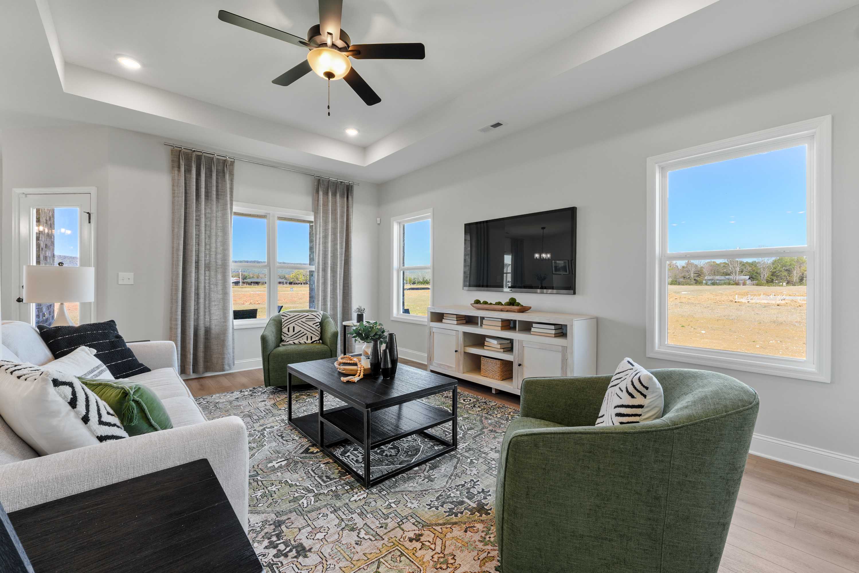 Cozy living room at Ramsay Cove in Owens Cross Roads Alabama with hardwood floors, large windows overlooking countryside, modern gray sofa and green chairs