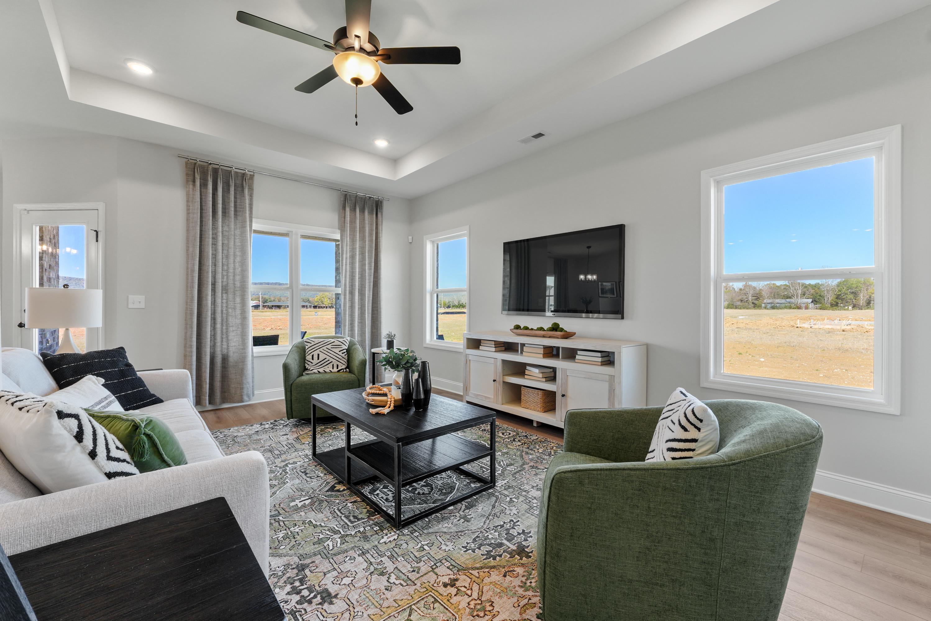 Cozy living room at Ramsay Cove in Owens Cross Roads Alabama with hardwood floors, large windows overlooking countryside, modern gray sofa and green chairs