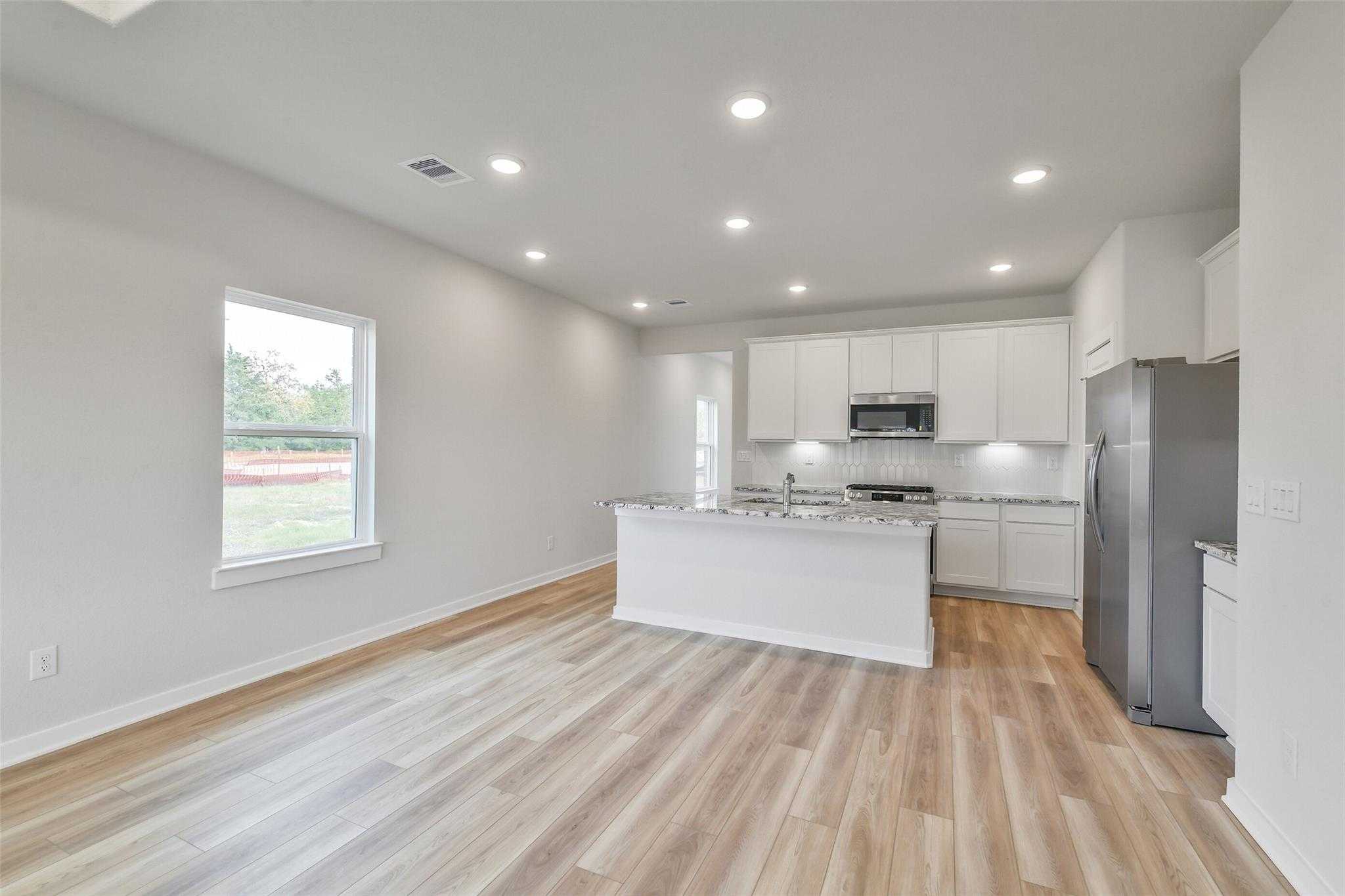 Modern open-concept kitchen with white cabinets, granite counters, and stainless appliances in Davidson Homes The Colorado G, Magnolia, Texas