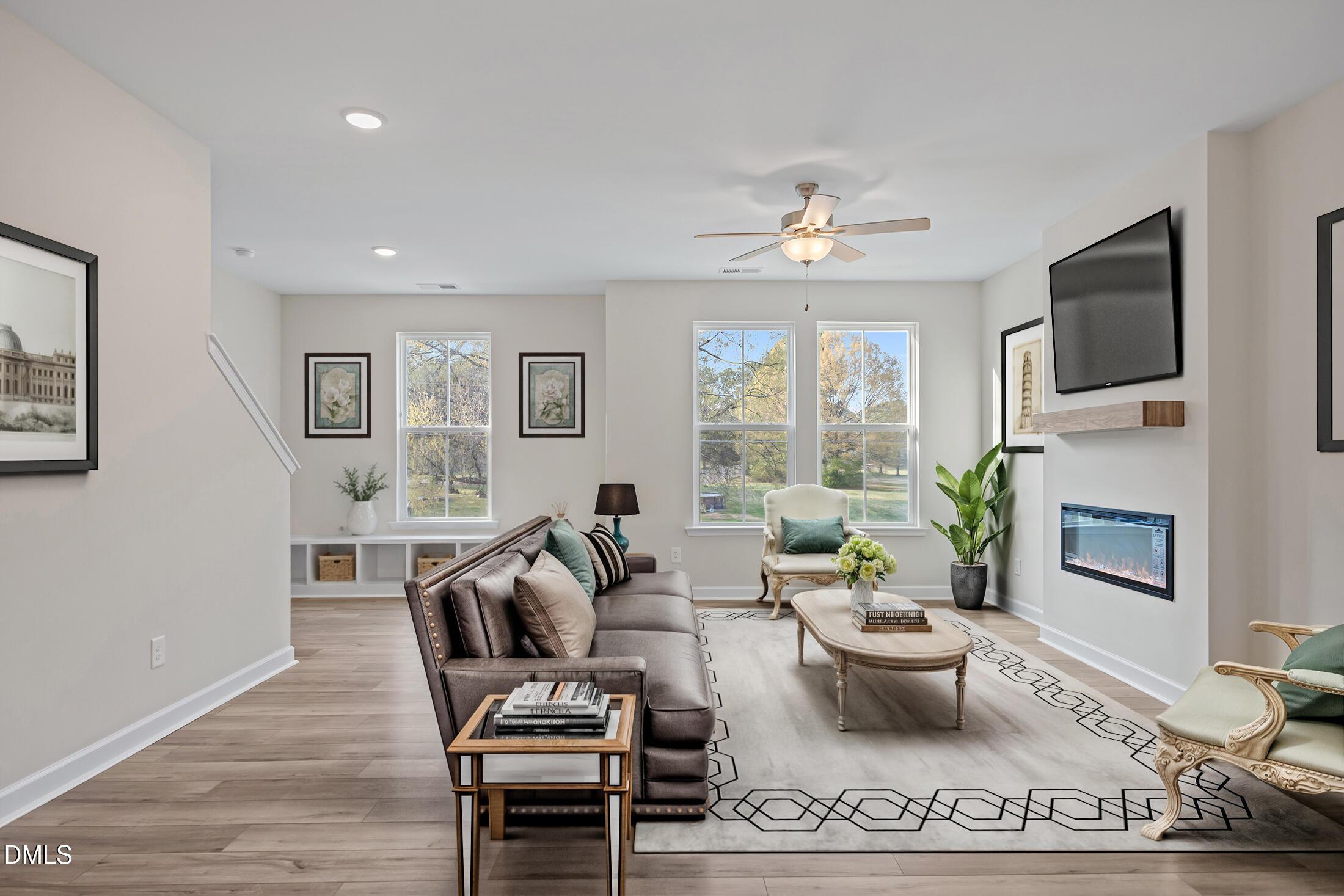 Elegant living room with leather sectional sofa, electric fireplace, mounted TV, large windows in The Avery by Davidson Homes, Knightdale, NC