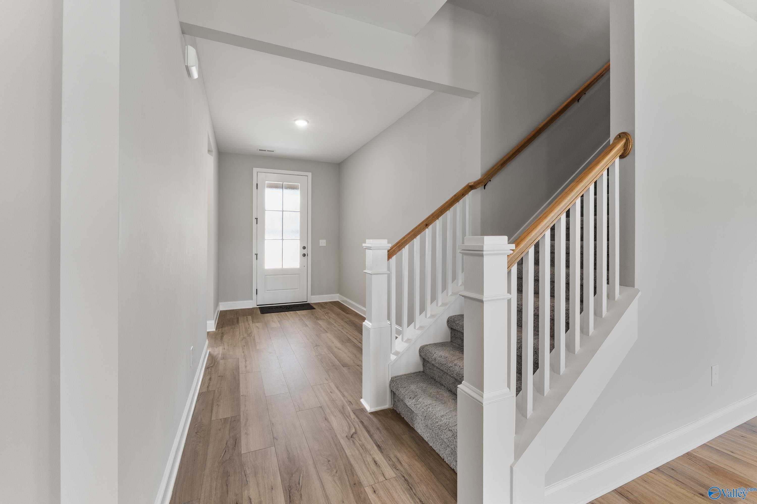 Elegant entry hallway with light gray walls, hardwood floors, and oak staircase in Davidson Homes The Montgomery B With Bonus, Toney, AL
