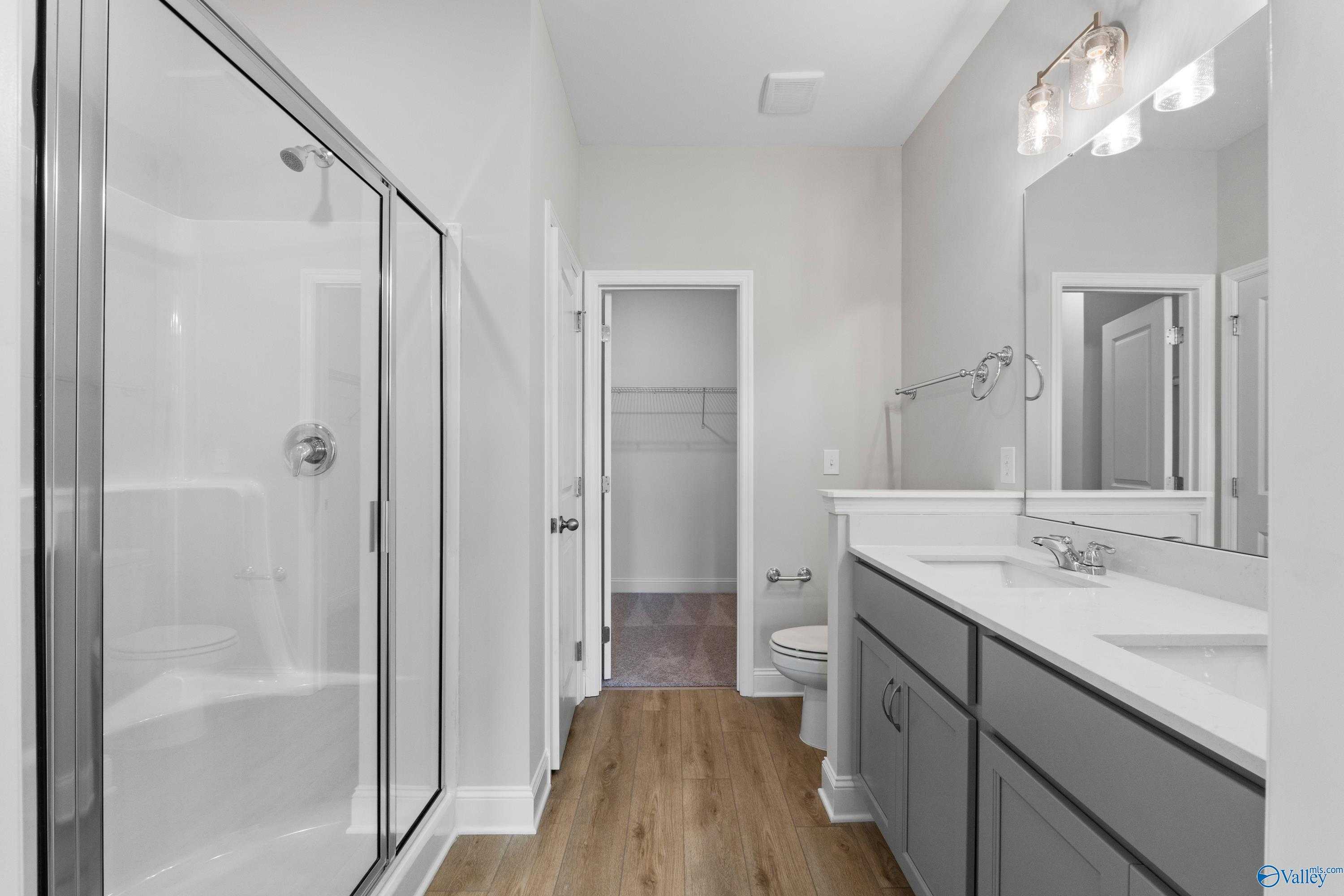Modern master bathroom with frameless glass shower, double vanity gray cabinets, and walk-in closet in Davidson Homes The Asheville, Meridianville, Alabama