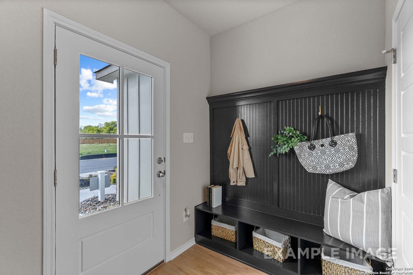 Stylish entry foyer with black shiplap bench, coat hooks, hanging purse, and sunny yard view through open glass door in Davidson Homes Sabine B, San Antonio