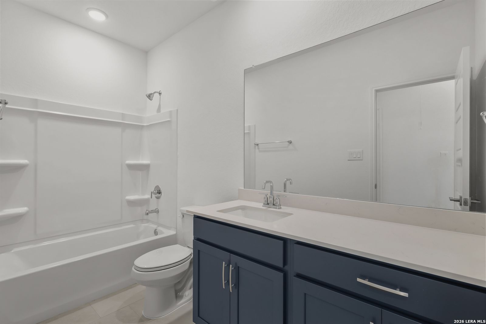 Bright guest bathroom featuring white tub-shower combo, navy cabinets, quartz vanity in Davidson Homes The Glenwood E, Elmendorf TX