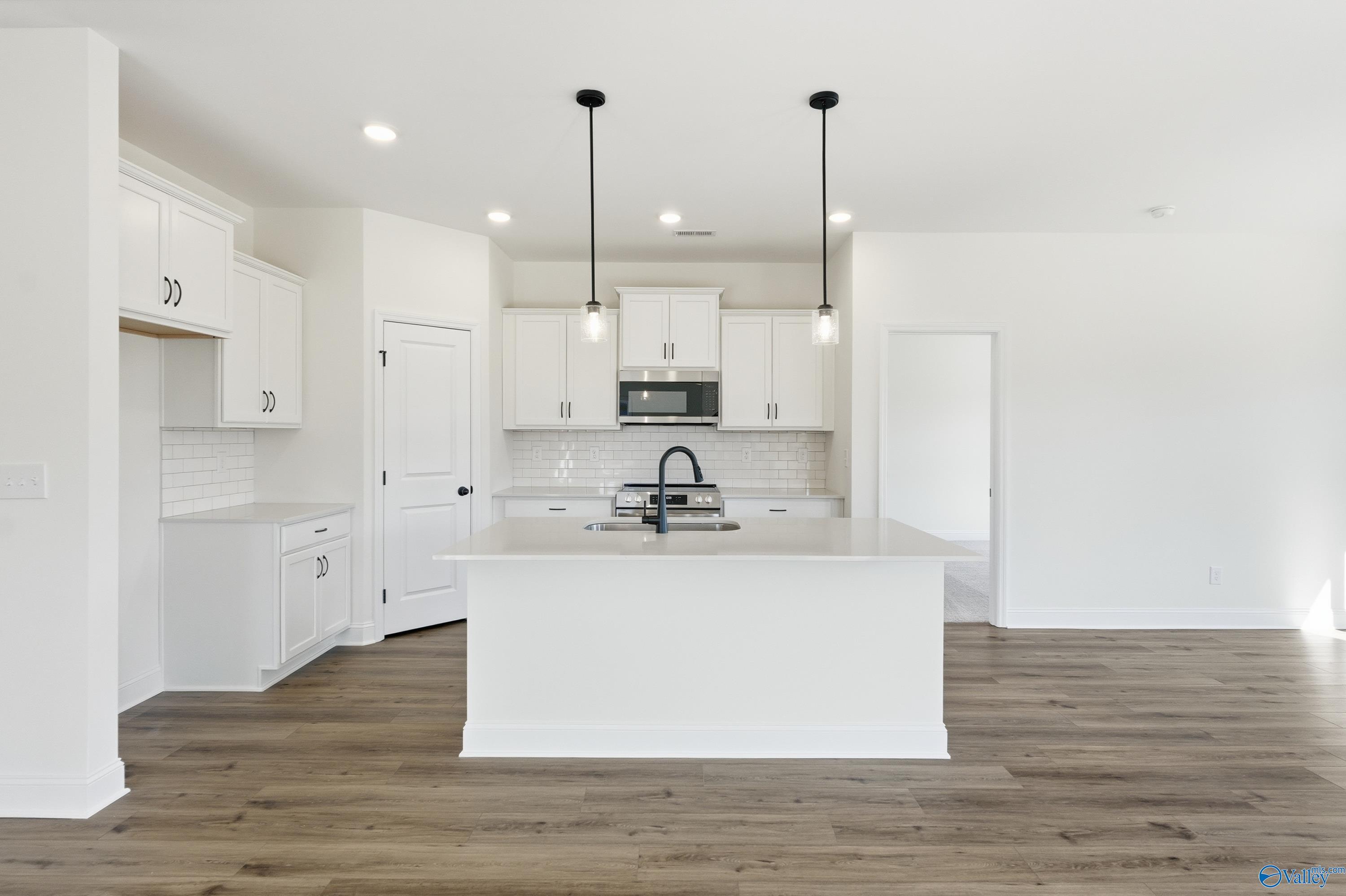 Modern white kitchen featuring large island, stainless appliances, subway tile backsplash in Davidson Homes The Franklin C, New Market, AL