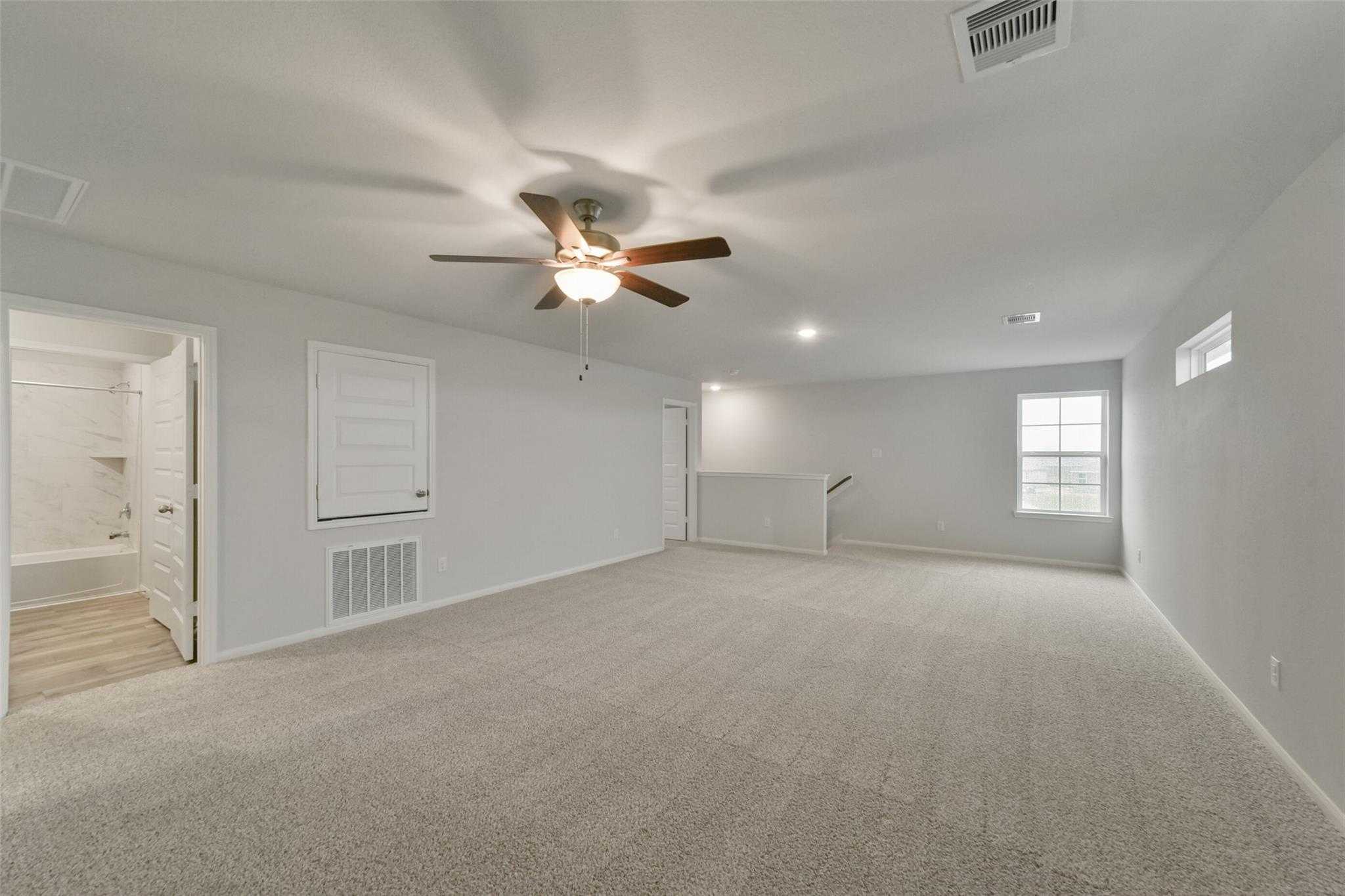Spacious upstairs bonus room with ceiling fan, carpet flooring, and adjacent baths in Davidson Homes The San Marcos E, Beasley, Texas