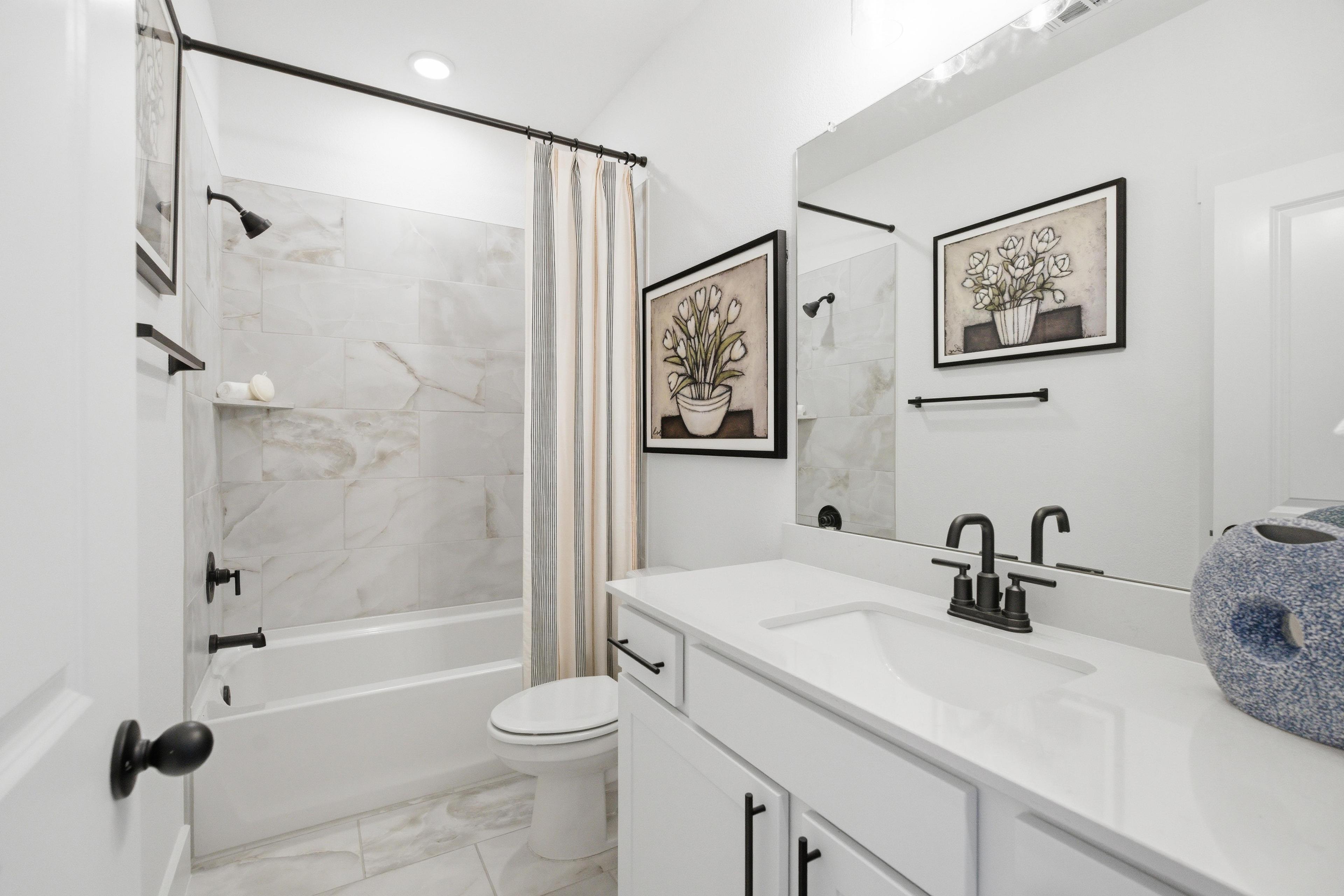 Spacious white bathroom at Mercer Meadows in Royse City Texas with marble shower, bathtub, vanity, and floral artwork