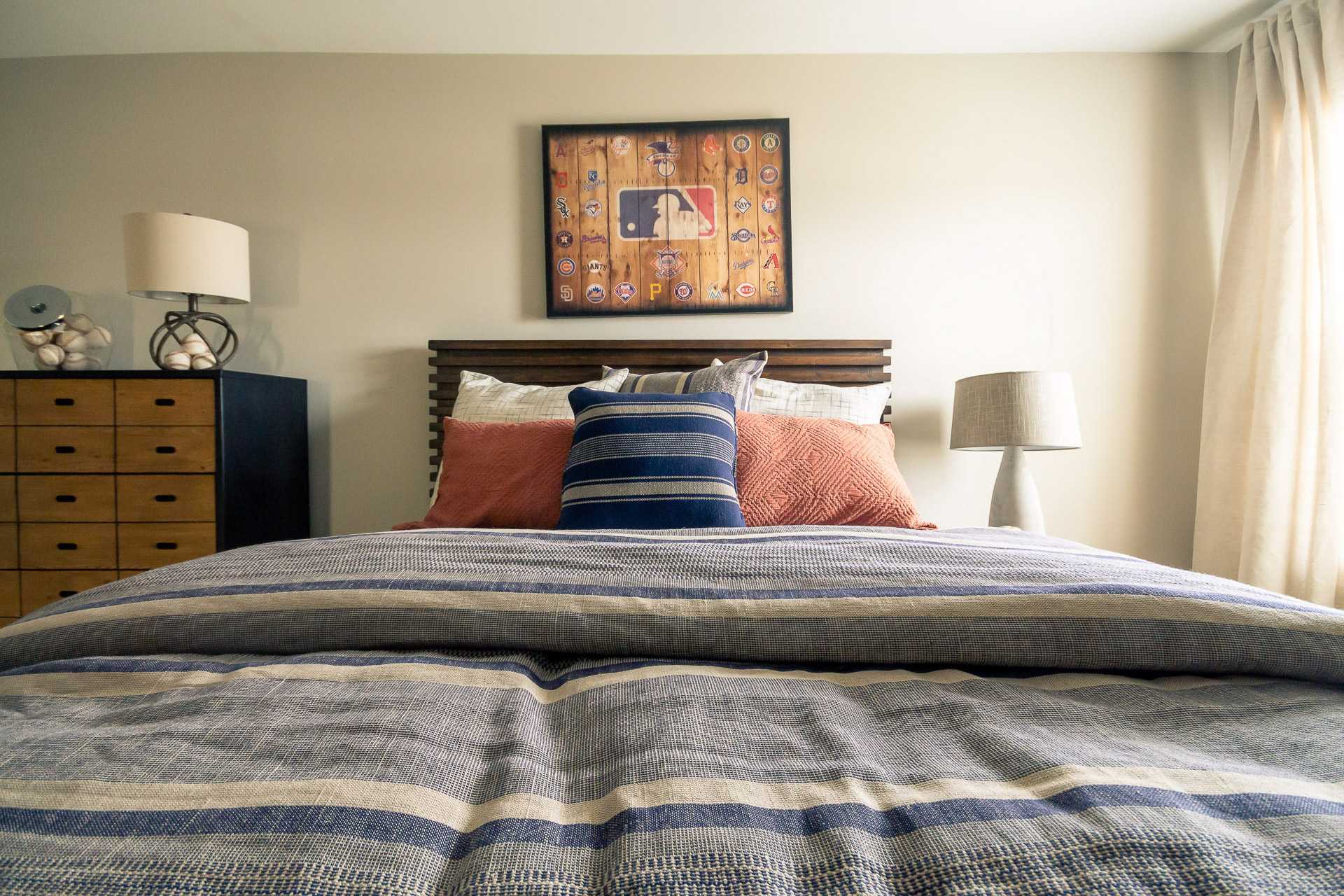 Cozy bedroom at Summer Pointe in Madison Alabama featuring gray striped bedding, blue pillows, wooden headboard, and MLB wall art