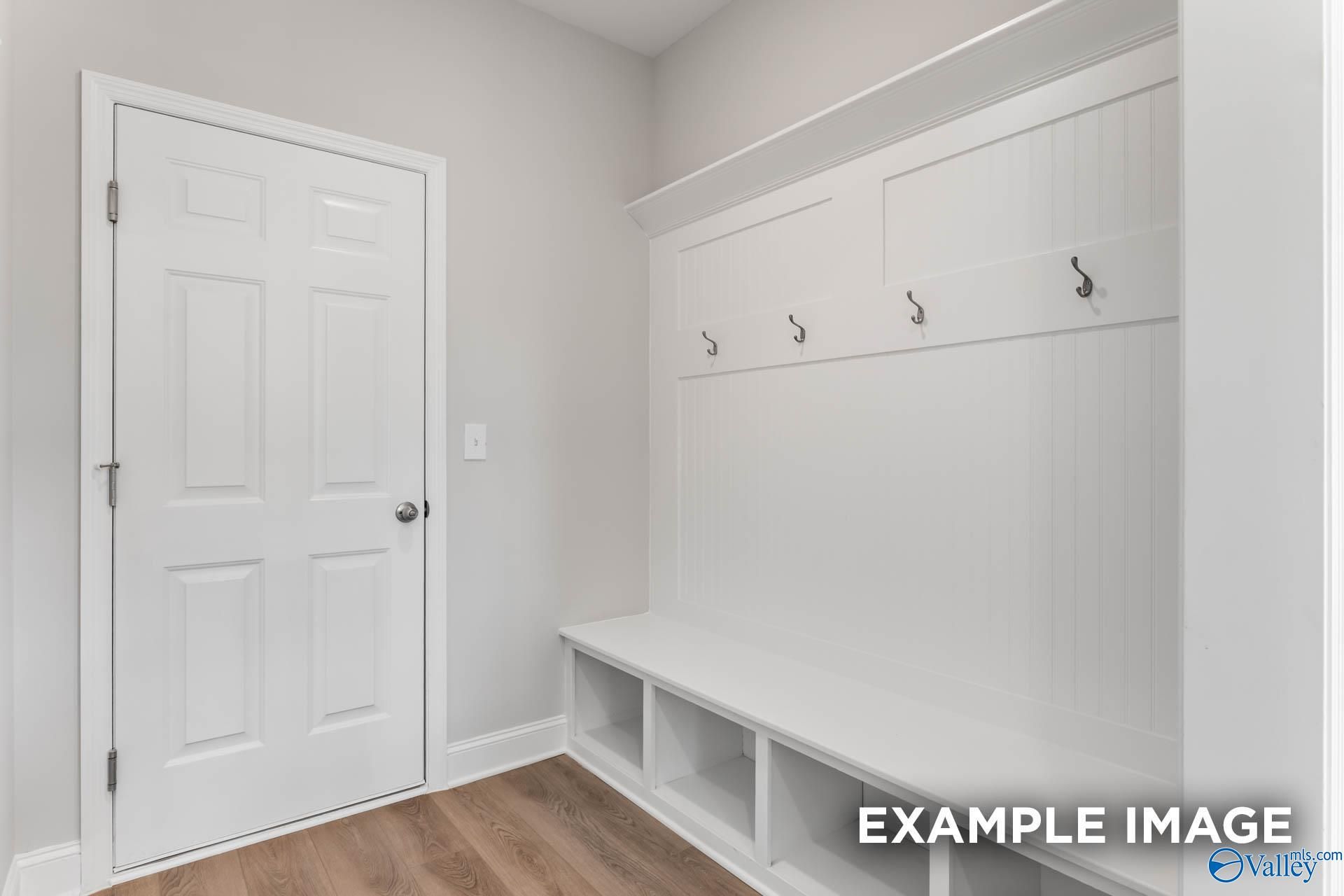 Custom mudroom with built-in white lockers, storage bench, coat hooks, and paneled door in Davidson Homes Chelsea D, New Market, Alabama