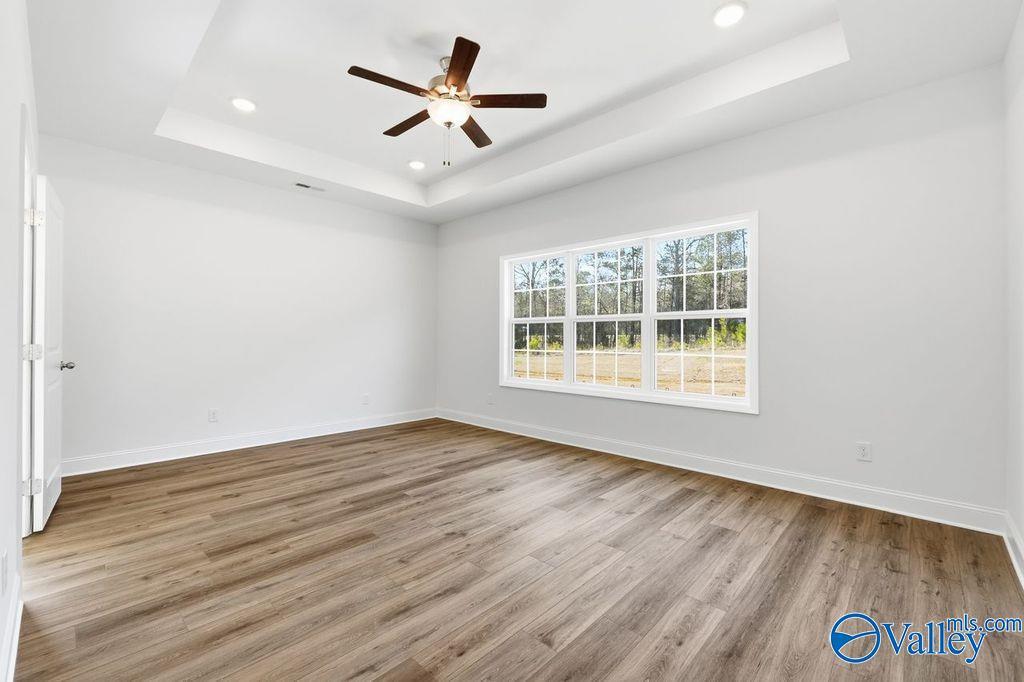 Bright bedroom with tray ceiling, ceiling fan, hardwood floors, and large windows in Davidson Homes The Montgomery, Hartselle, Alabama