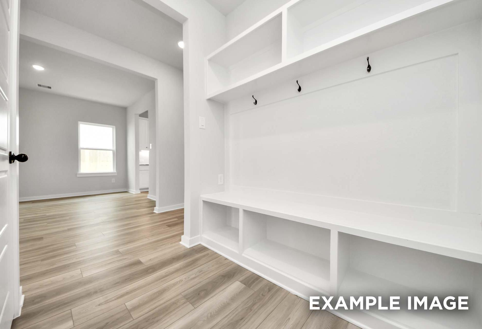 Built-in white mudroom bench with storage and hooks in The Sorrento home design featuring wood-look flooring.