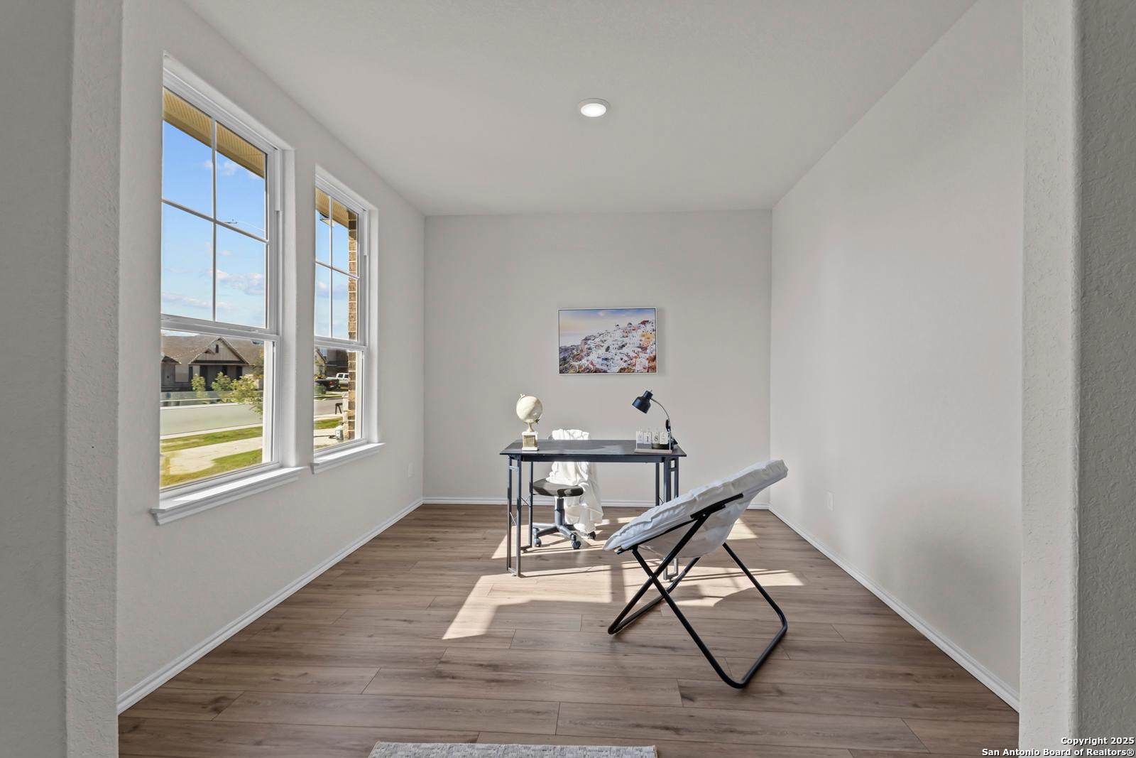 Bright home office with wooden desk, lamp, and abstract art on white walls, natural light via large windows in Davidson Homes The Douglas C, Seguin, Texas