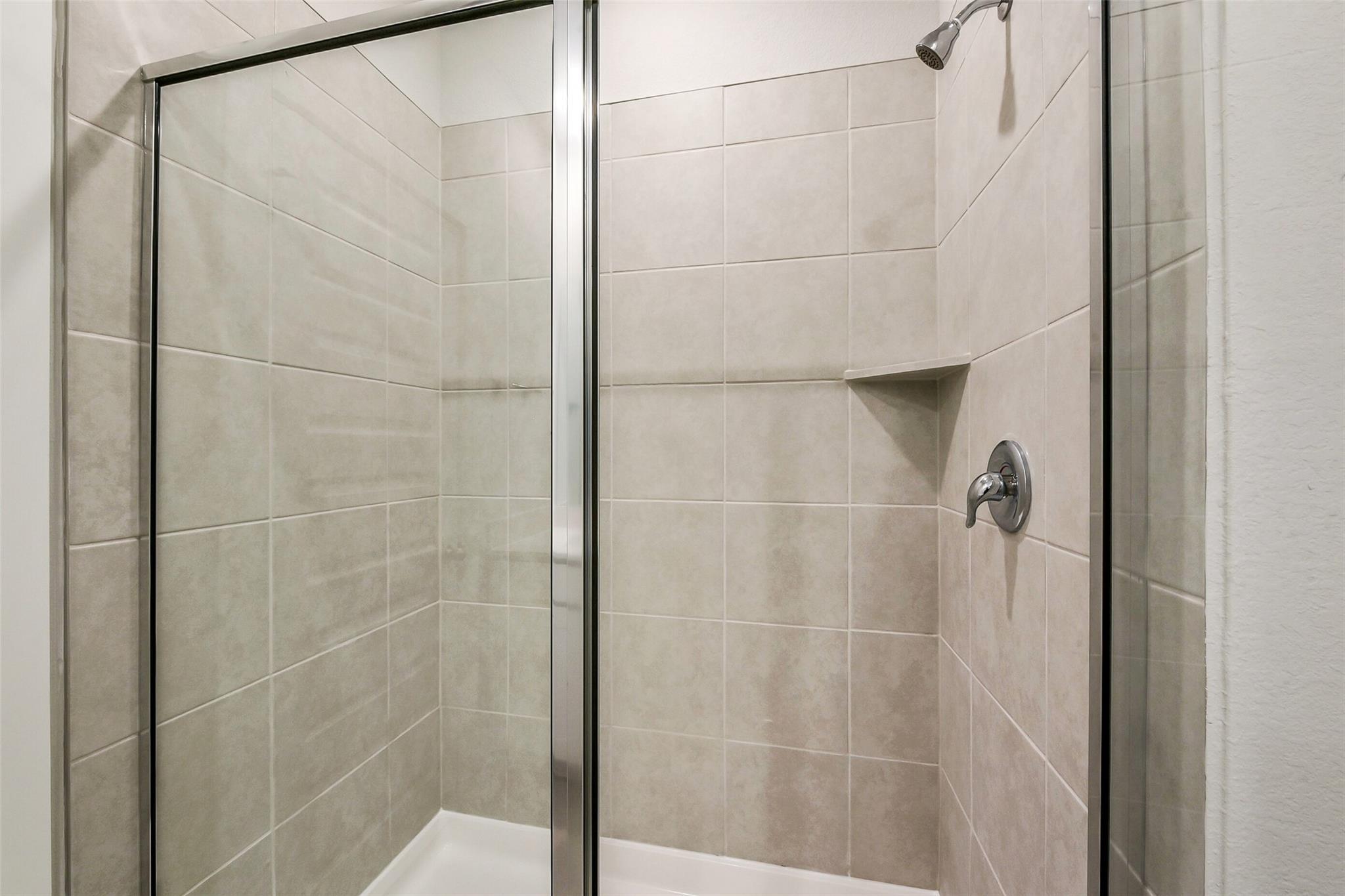 Modern frameless glass shower enclosure with subway tile walls and niche in Davidson Homes The Frio G master bath, Dayton, Texas