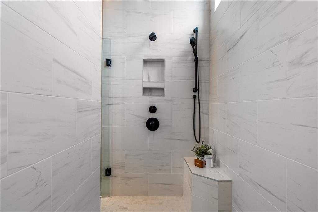 Modern walk-in shower with white subway tiles, black rain showerhead, glass enclosure, and niche shelf in The Seaside B master bath, Woodstock, GA
