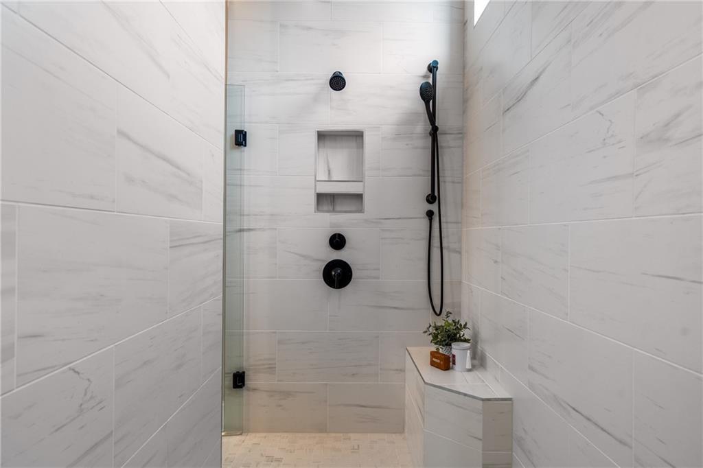 Modern walk-in shower with white subway tiles, black rain showerhead, glass enclosure, and niche shelf in The Seaside B master bath, Woodstock, GA