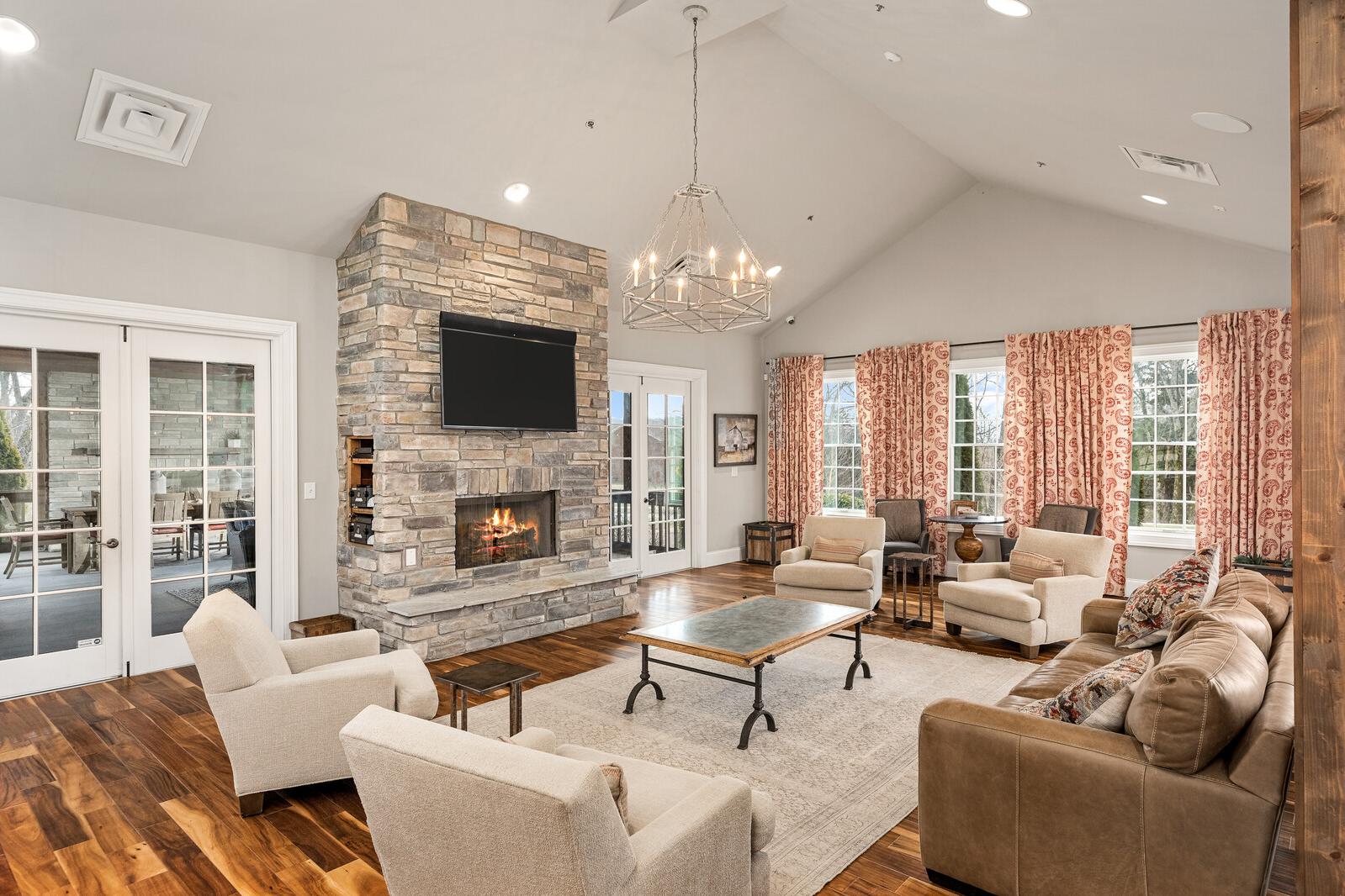 Cozy community lounge at Carellton in Gallatin TN with stone fireplace, leather sofas, chandelier, and French doors to patio