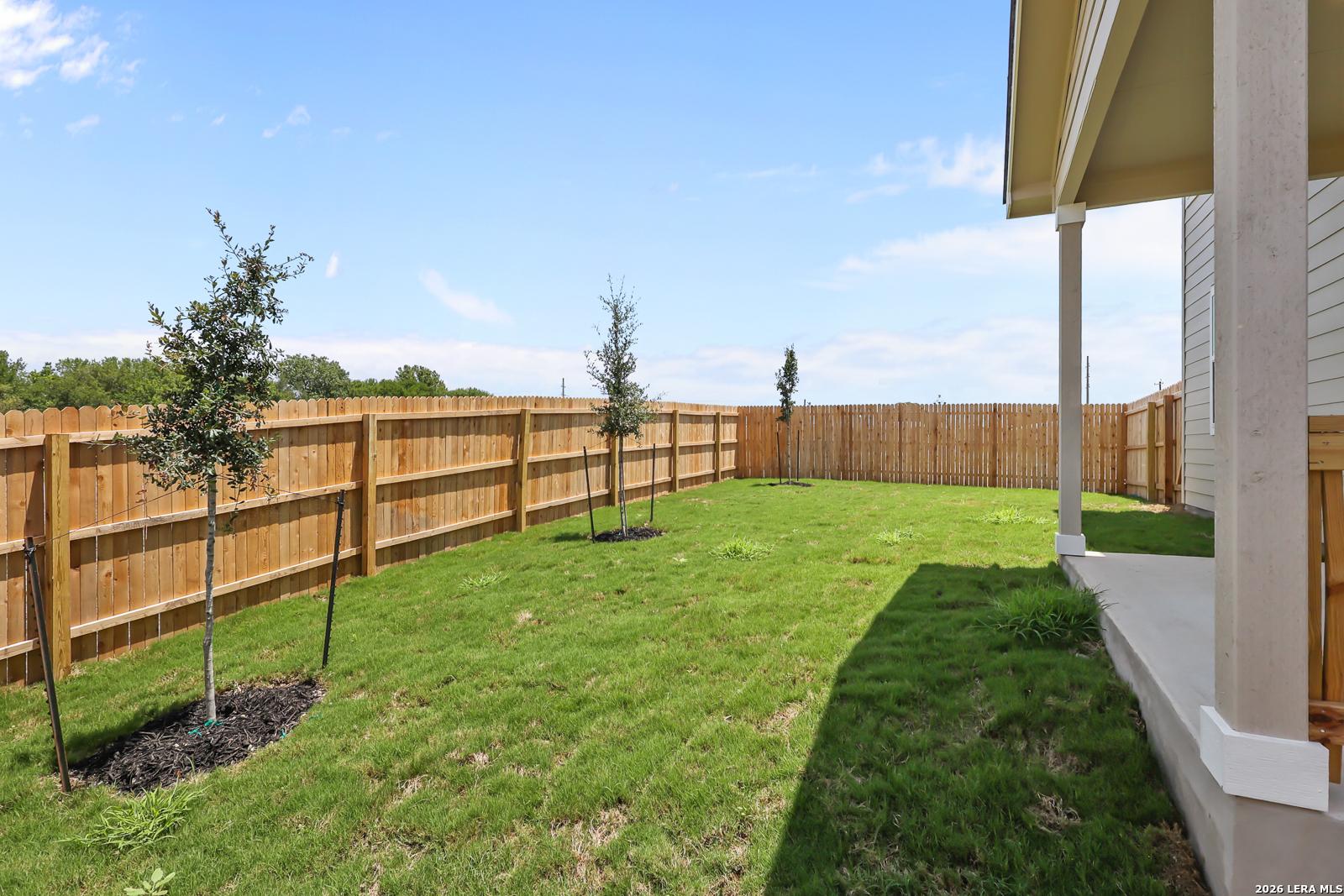Private backyard with a covered patio, wooden fence, and young trees at a Davidson Homes property in Rayburn Valley, TX.