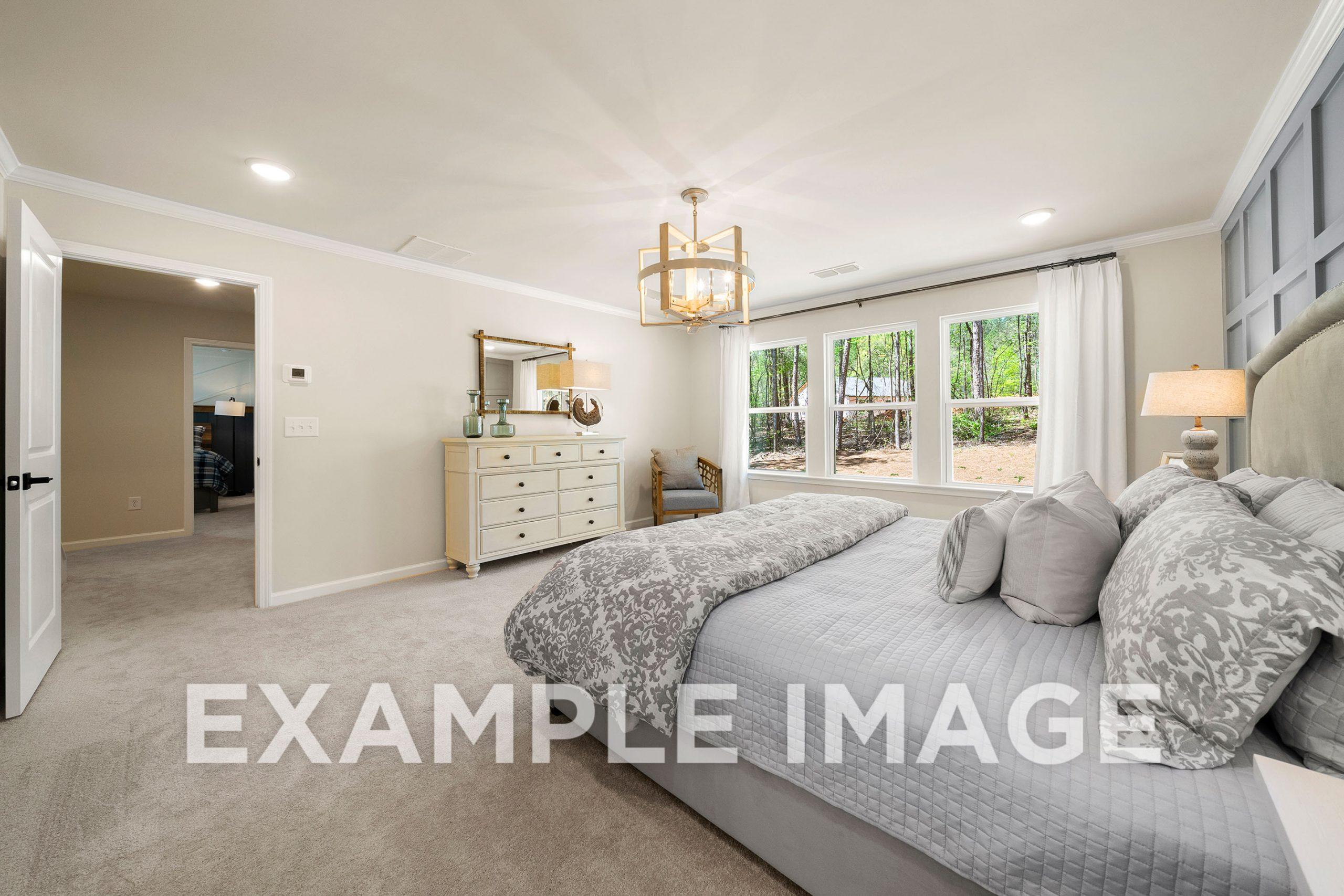 Spacious master bedroom in The Hickory B featuring king bed, chandelier, dresser, and large windows with tree views
