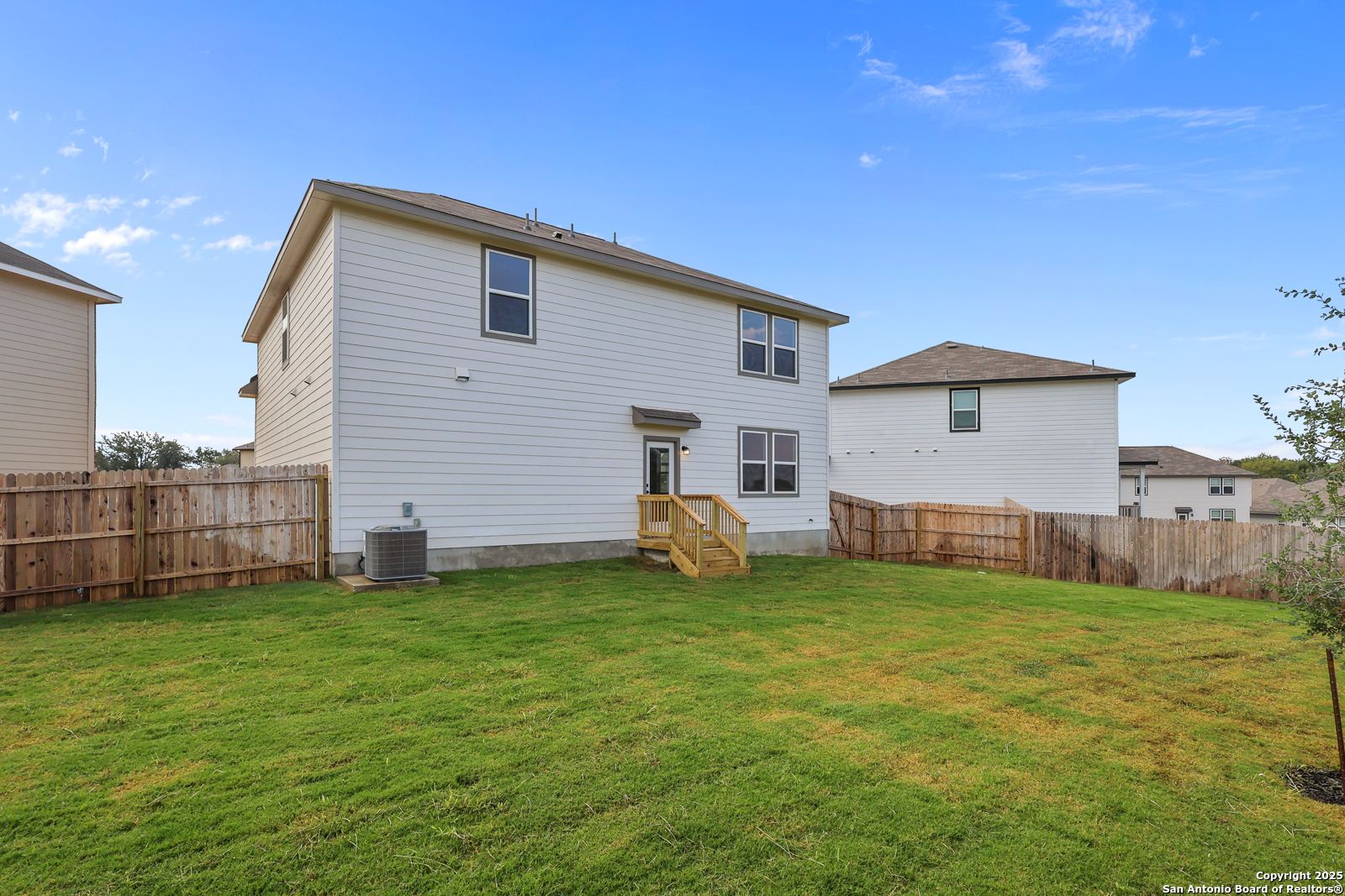 Backyard of two-story white 4-bedroom Murray J home with covered deck, wooden stairs, and fenced grassy yard in Royal Crest, San Antonio