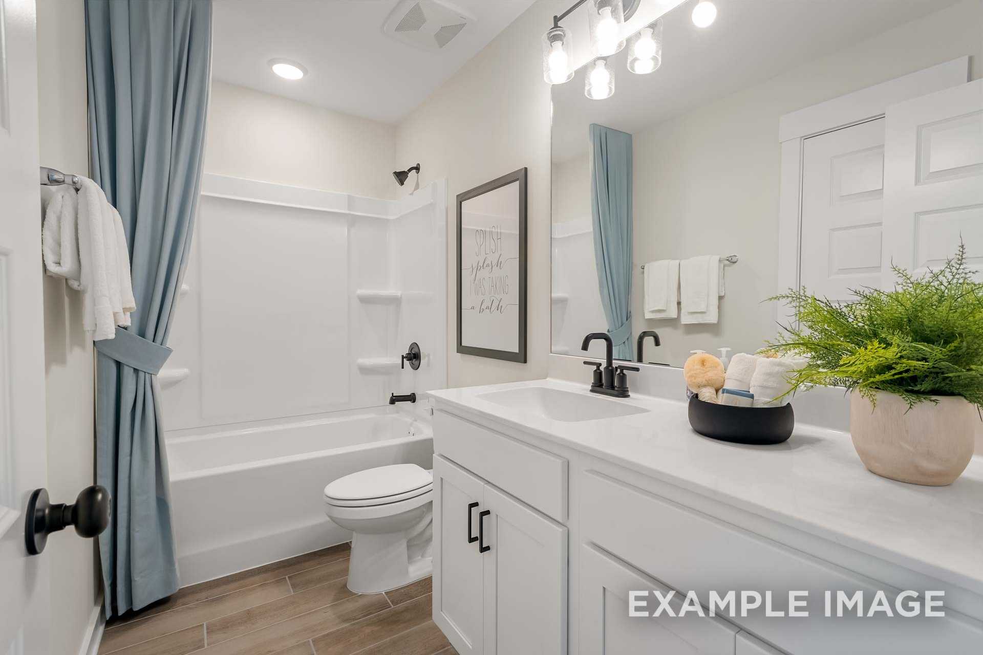 Spacious master bathroom in The Ridgeport B with white subway tile shower, deep soaking tub, modern vanity, blue curtains, and hardwood floors