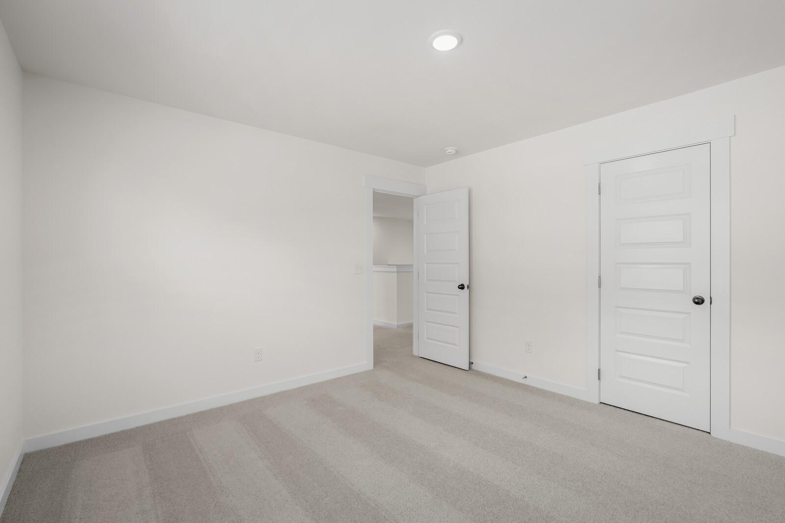 Spacious bedroom with neutral carpet and white walls in The Willow floor plan at Woods Crossing, Gallatin, Tennessee.