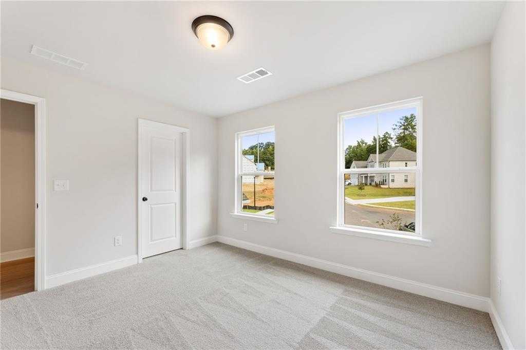Bright bedroom with neutral walls, carpet flooring, and windows overlooking neighborhood in Davidson Homes The Hickory B, Buford, GA