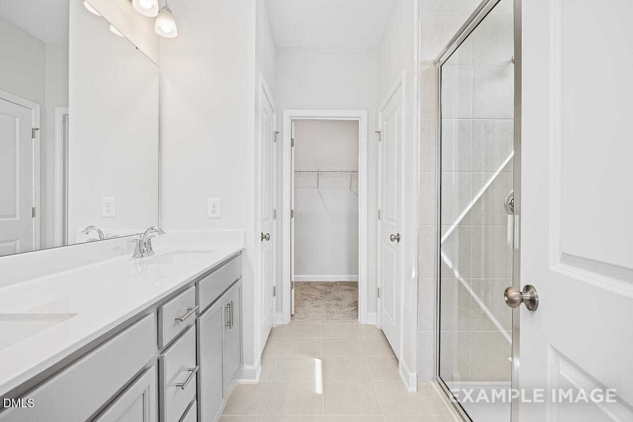 Modern master bathroom featuring double vanity, walk-in closet, and frameless glass shower in Davidson Homes The Daphne C, Lillington, NC