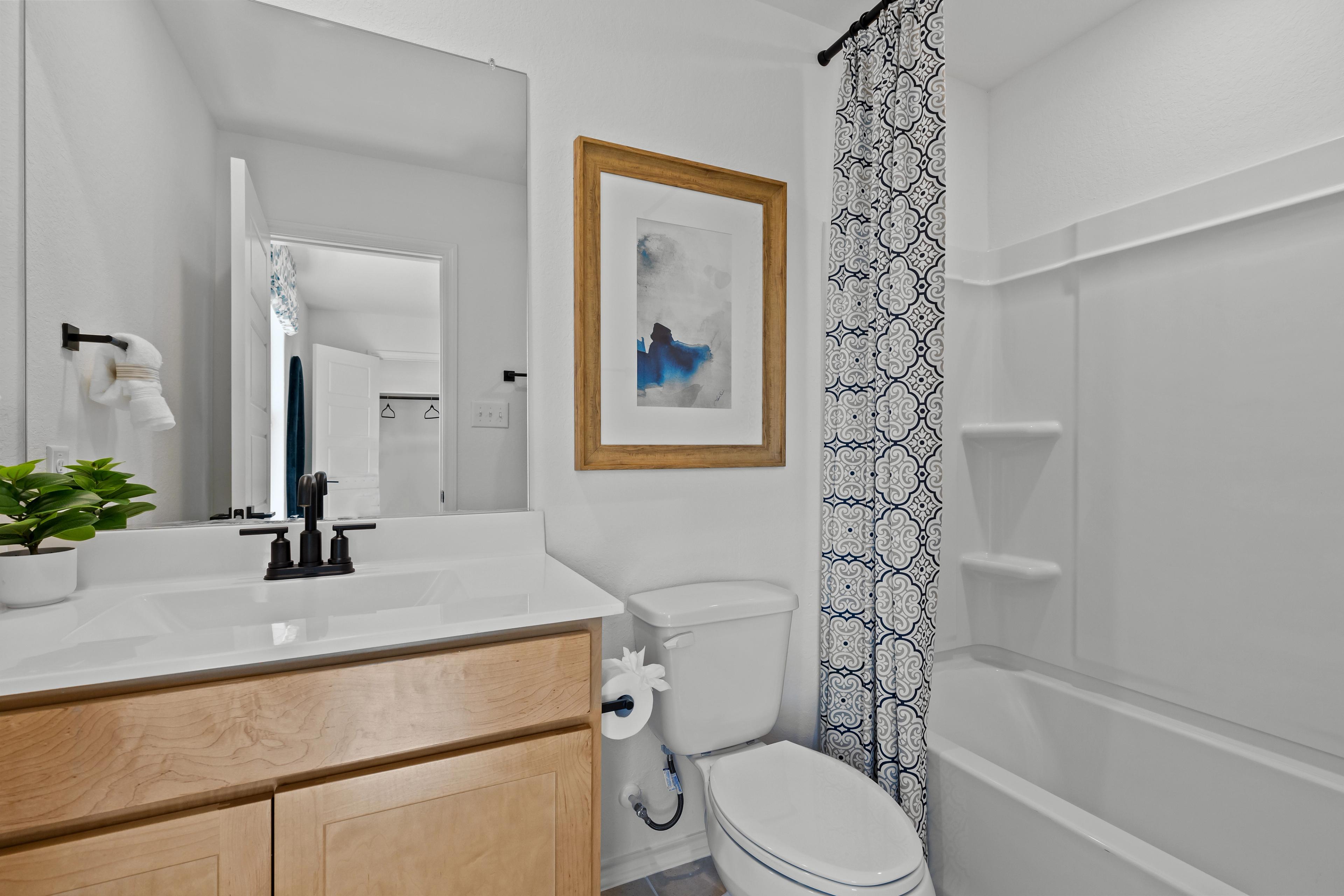 Spacious bathroom in The Douglas F by Davidson Homes featuring white vanity sink, soaking tub with blue patterned curtain, and framed abstract art