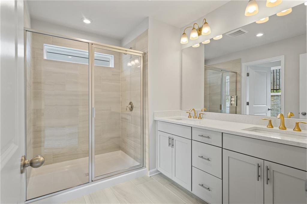 Modern master bathroom featuring frameless glass shower, double vanity with gold fixtures in Davidson Homes The Marion B, Kennesaw, GA