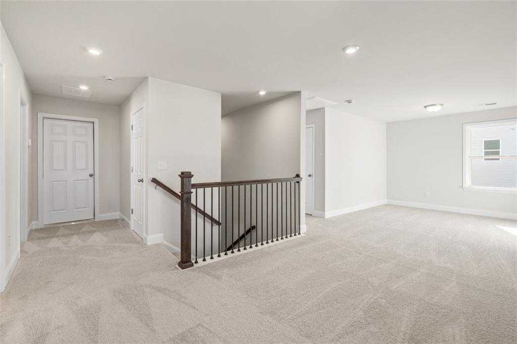 Spacious carpeted upstairs hallway with wooden staircase railing and bedroom doors in Davidson Homes The Ash C, Wehunt Meadows, Hoschton