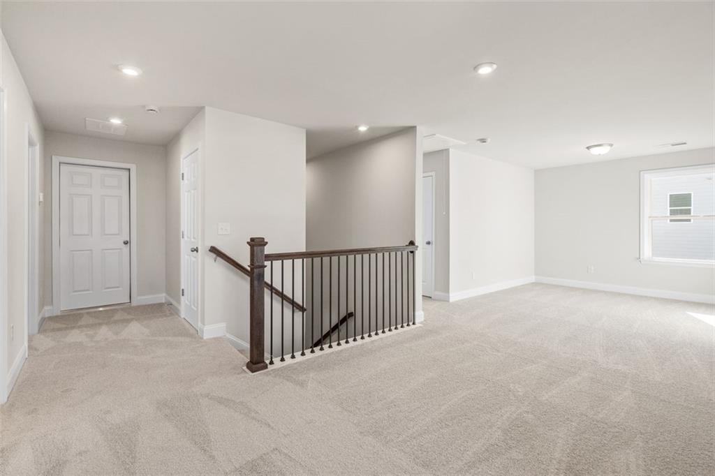 Spacious carpeted upstairs hallway with wooden staircase railing and bedroom doors in Davidson Homes The Ash C, Wehunt Meadows, Hoschton
