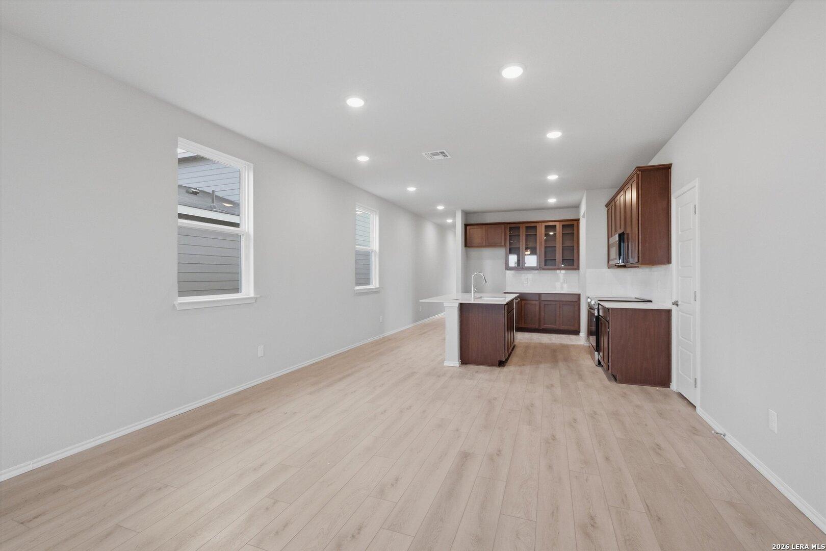Open-concept kitchen and living area with light oak floors, dark cabinets, white island in The Frio B home, Agave, San Antonio