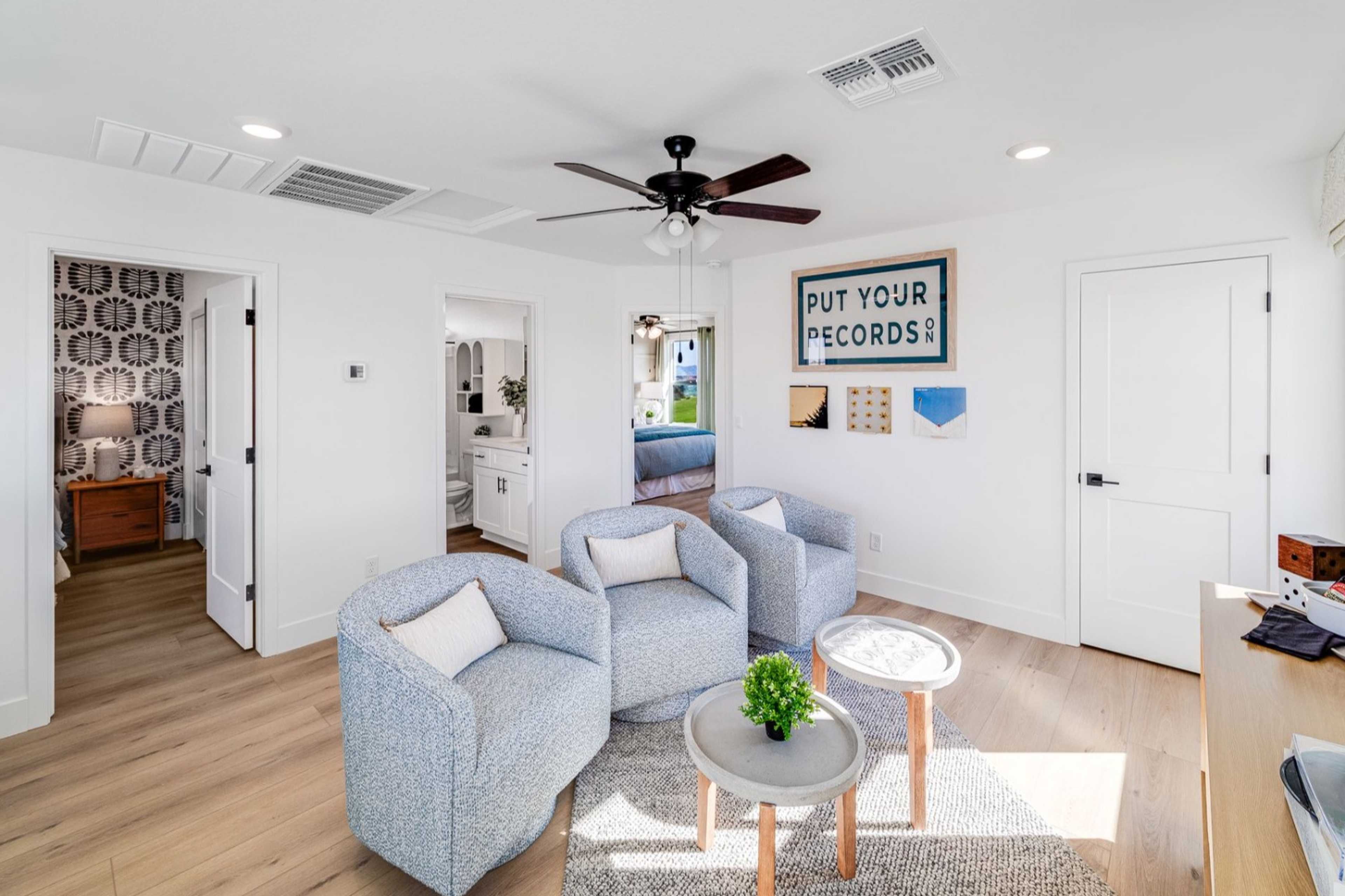 Upper floor sitting area in The Wilmington B showcasing blue armchairs, round table, plant, and open master suite access