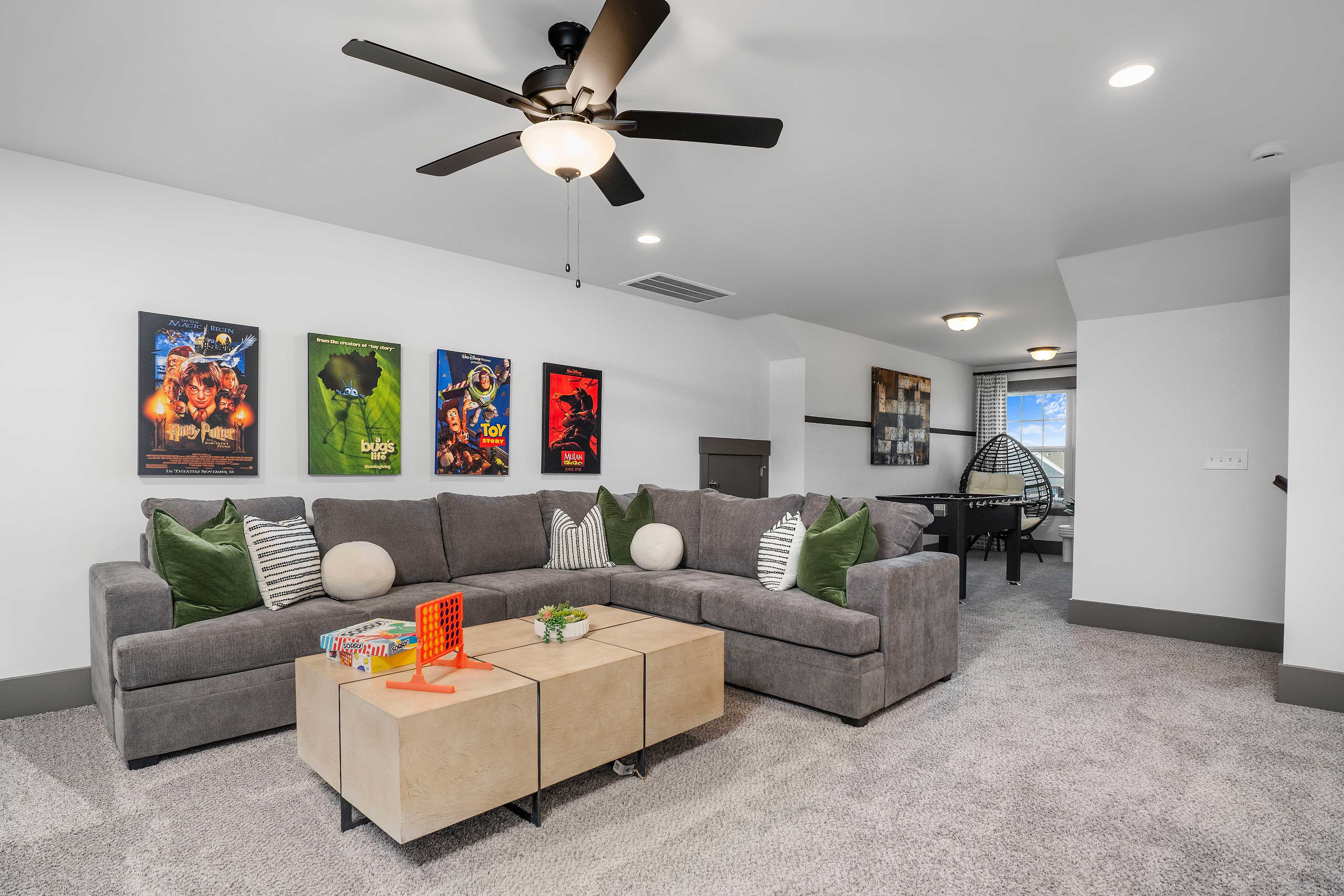 Cozy bonus room with gray sectional sofa, superhero movie posters, ceiling fans, and coffee table in Barnett's Crossing, Madison, Alabama