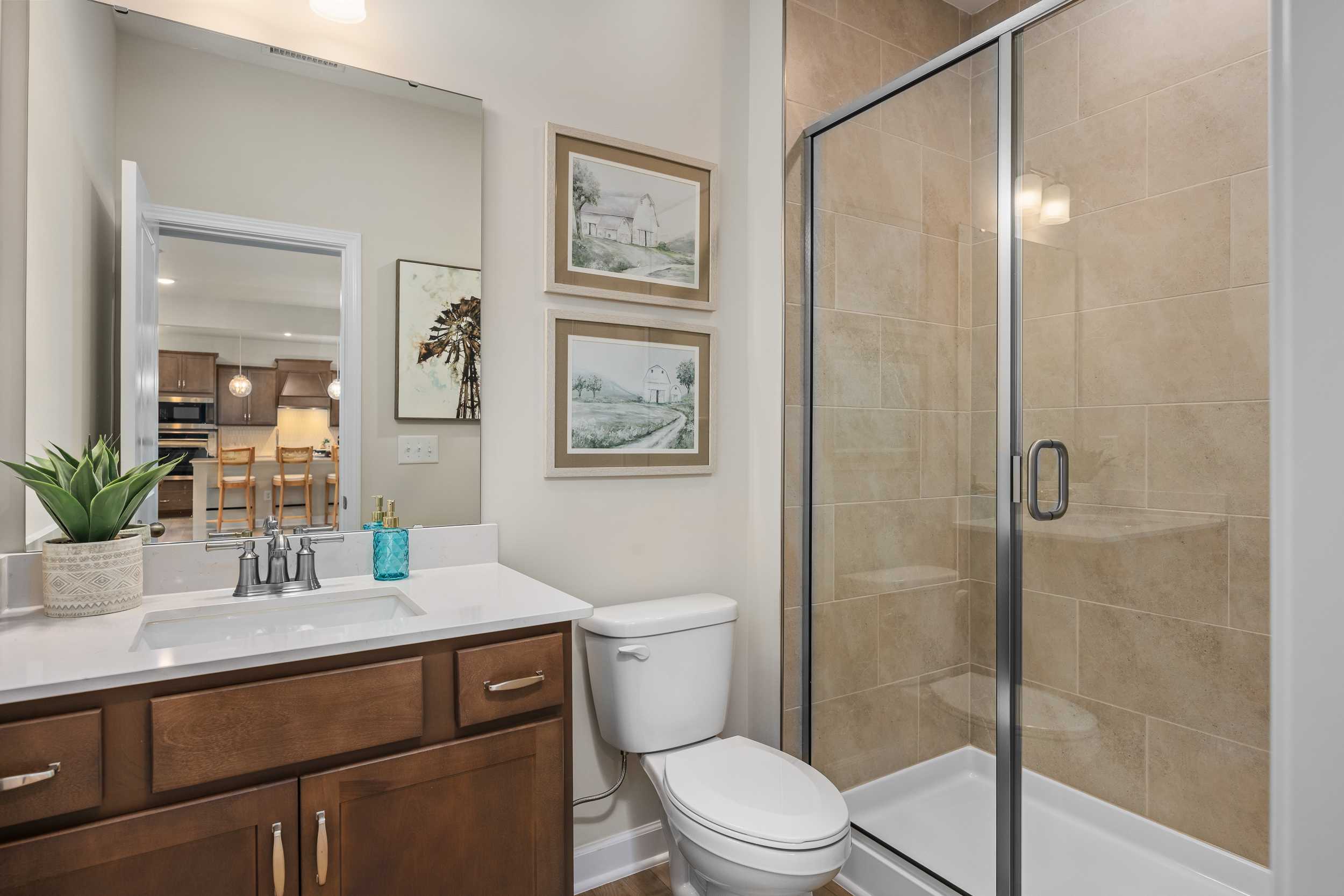 Master bathroom in The Willow G with wooden vanity, glass walk-in shower, neutral tiles, and framed art by Davidson Homes