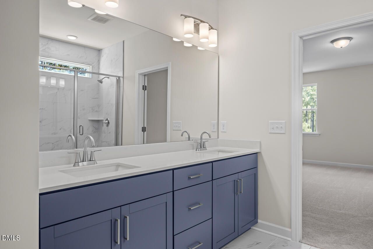 Modern bathroom with blue double vanity, quartz countertops, and walk-in shower in Davidson Homes Hickory II B floor plan.