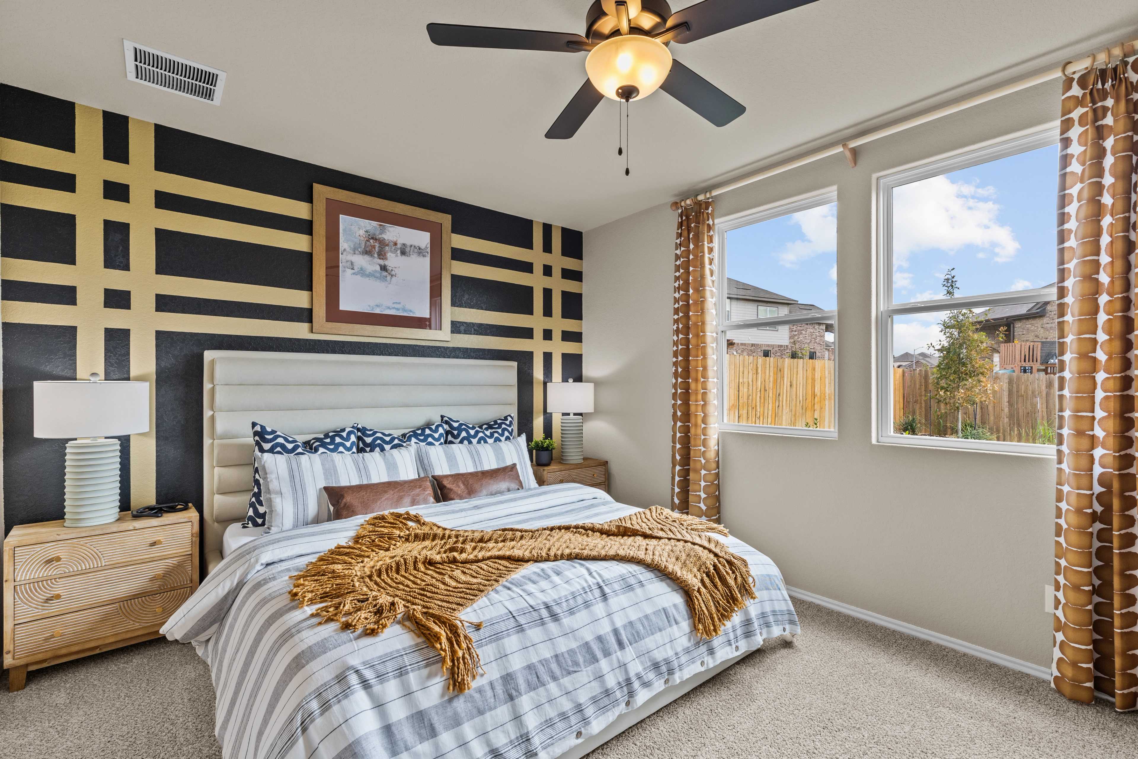 Spacious master bedroom at Bricewood in San Antonio Texas with black-yellow striped accent wall, plush bed, and large window views