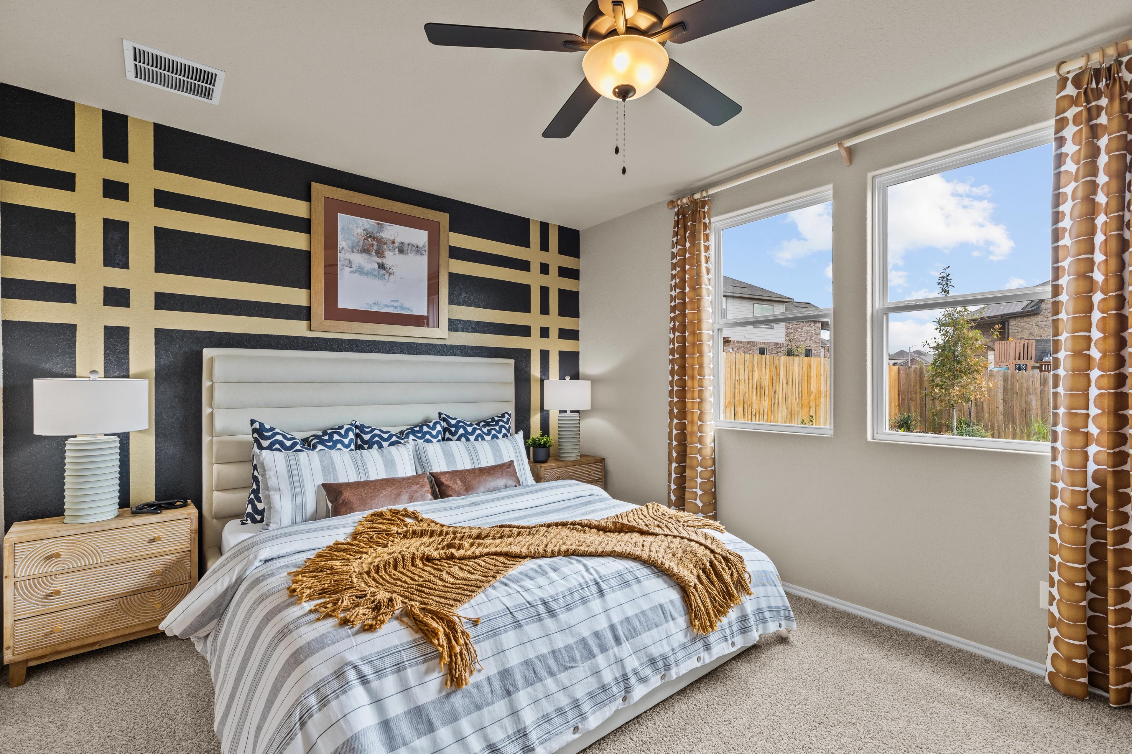 Spacious master bedroom at Bricewood in San Antonio Texas with black-yellow striped accent wall, plush bed, and large window views