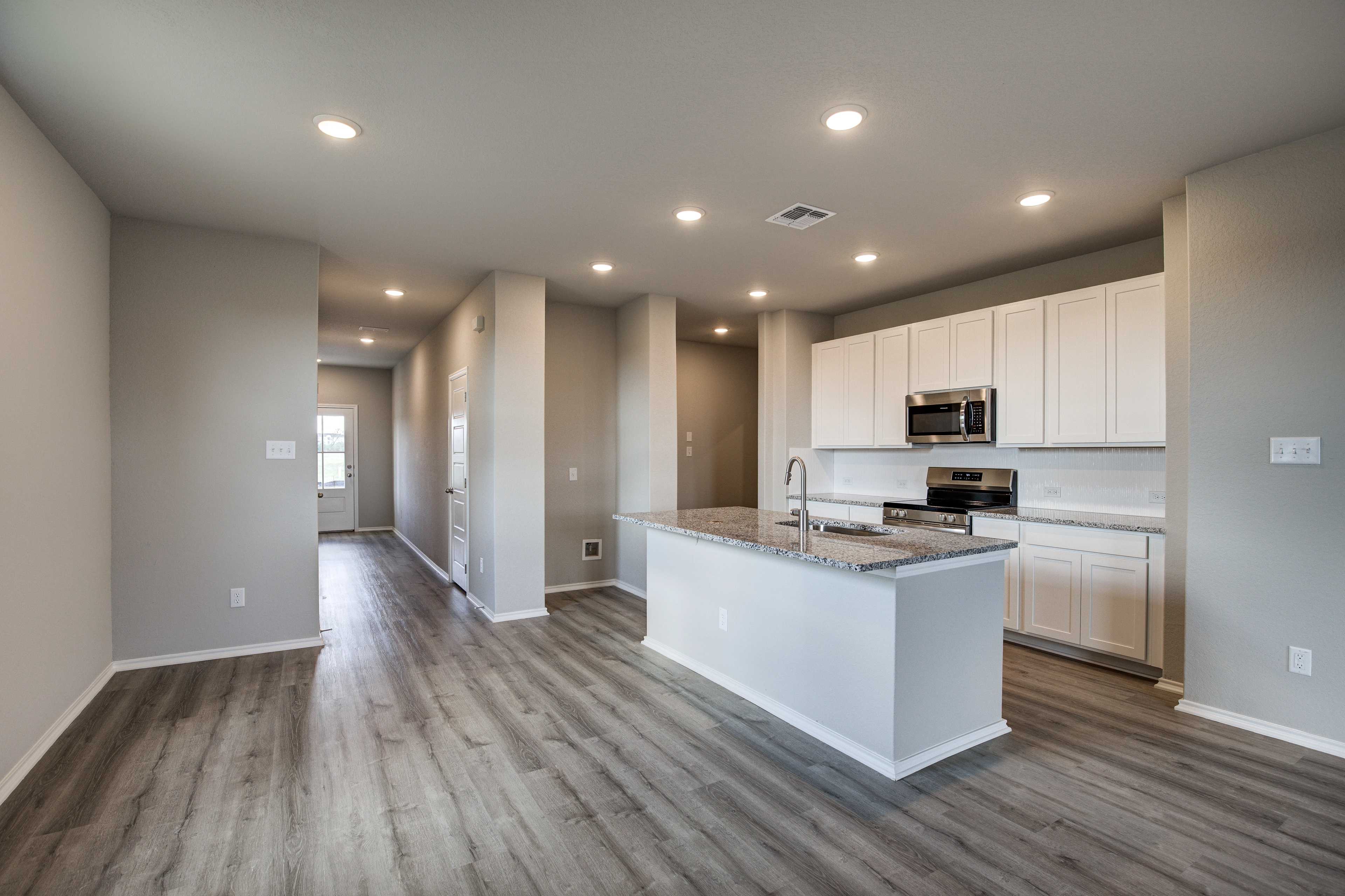 Spacious open-concept kitchen in The Blanco B home design with white cabinetry, granite island, stainless appliances, and hardwood floors