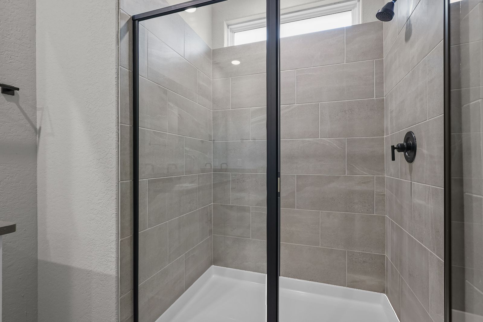 Modern walk-in shower with neutral tile surround and matte black fixtures in The Glenwood master suite.