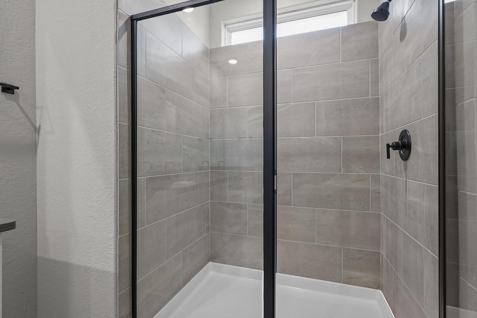 Modern walk-in shower with neutral tile surround and matte black fixtures in The Glenwood master suite.