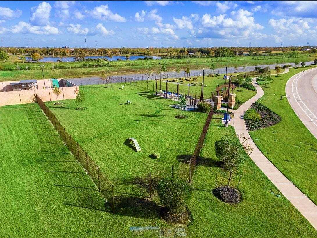 Aerial view of fenced playground with climbing structures, walking paths, and lush green space near pond in Sierra Vista, Rosharon, Texas
