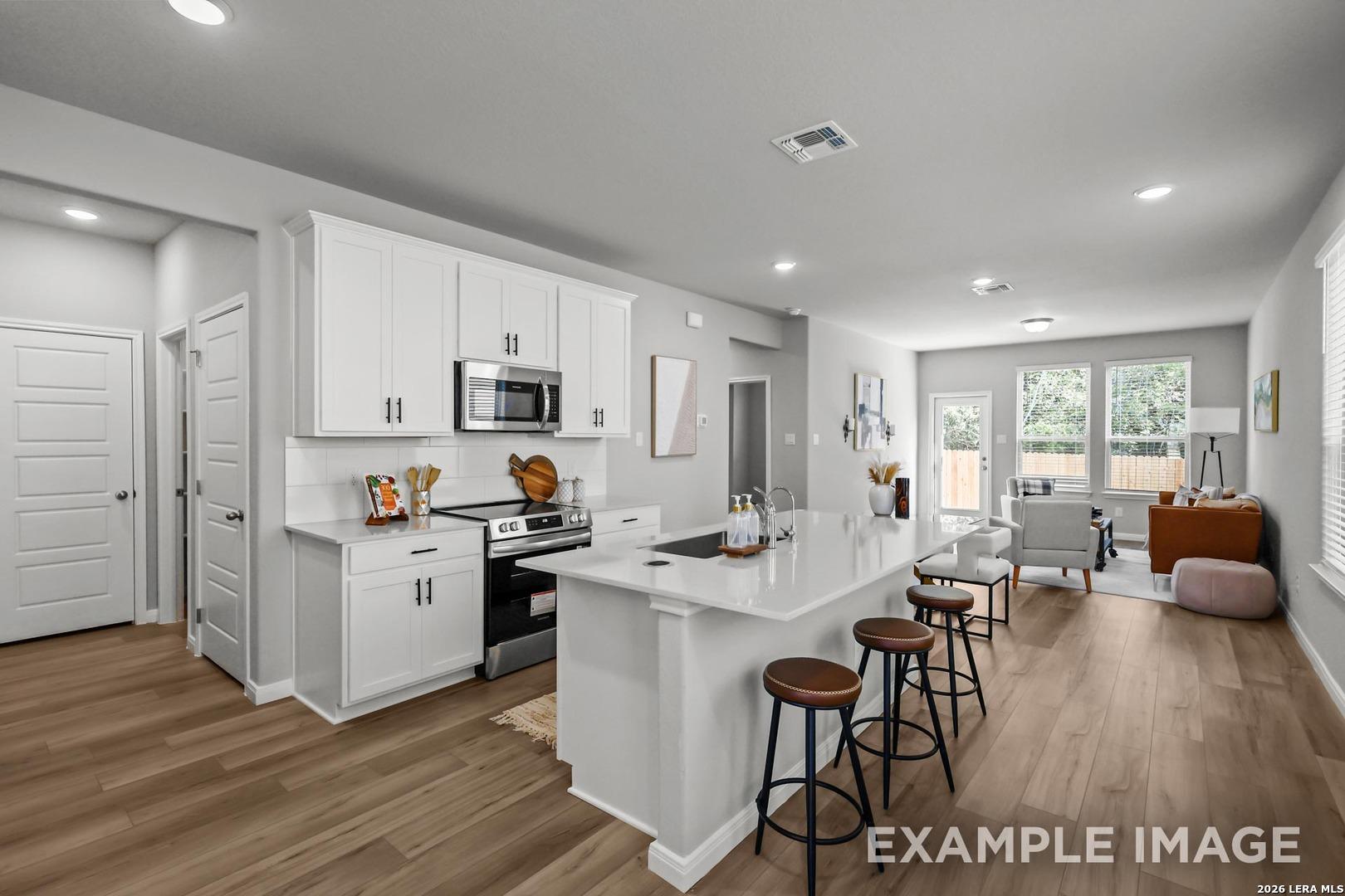 Open-concept kitchen with white cabinets, island seating, and stainless steel appliances in The Gillian A, Cedar Heights.