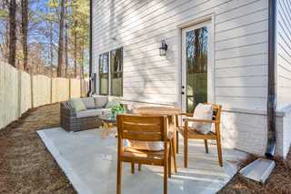 Cozy backyard patio of The Washington H townhome in Marietta featuring wicker sofa, wooden dining set, and white siding exterior