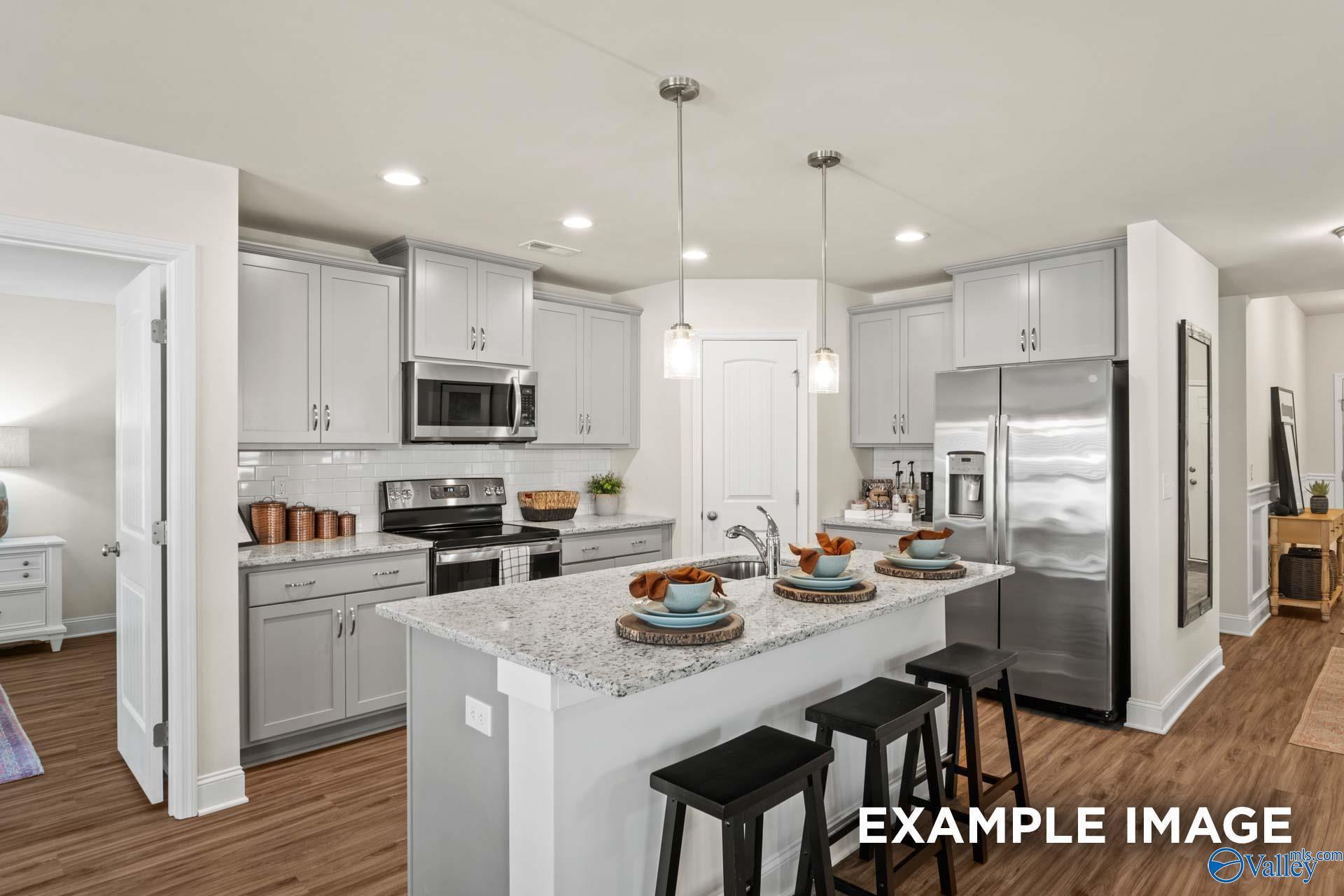 Modern kitchen featuring white shaker cabinets, granite countertops, stainless steel appliances, and island bar in Davidson Homes The Franklin C, Hazel Green, Alabama