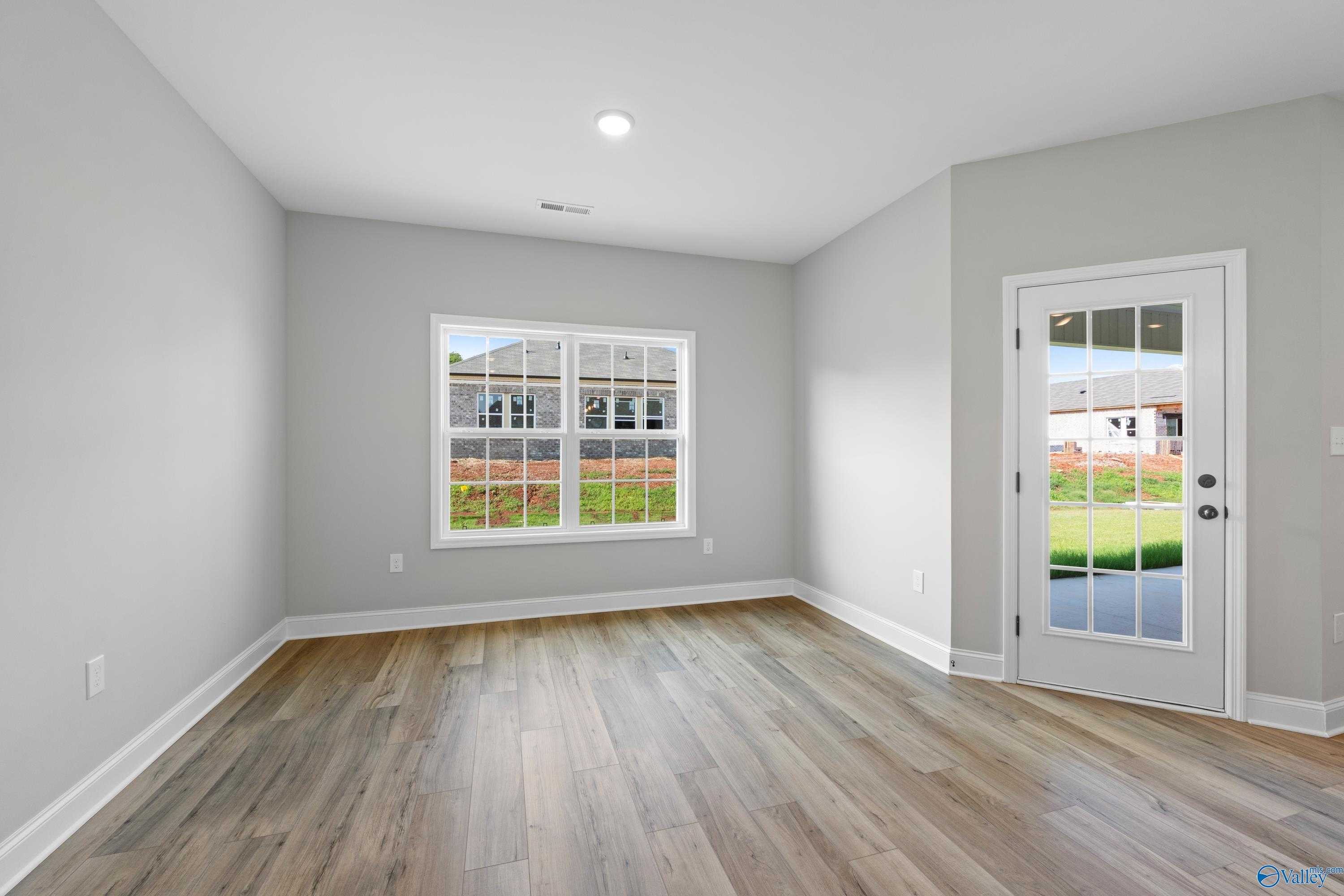 Bright empty bonus room with hardwood floors, large window, and glass door to green backyard in Davidson Homes The Rockford, Toney, Alabama