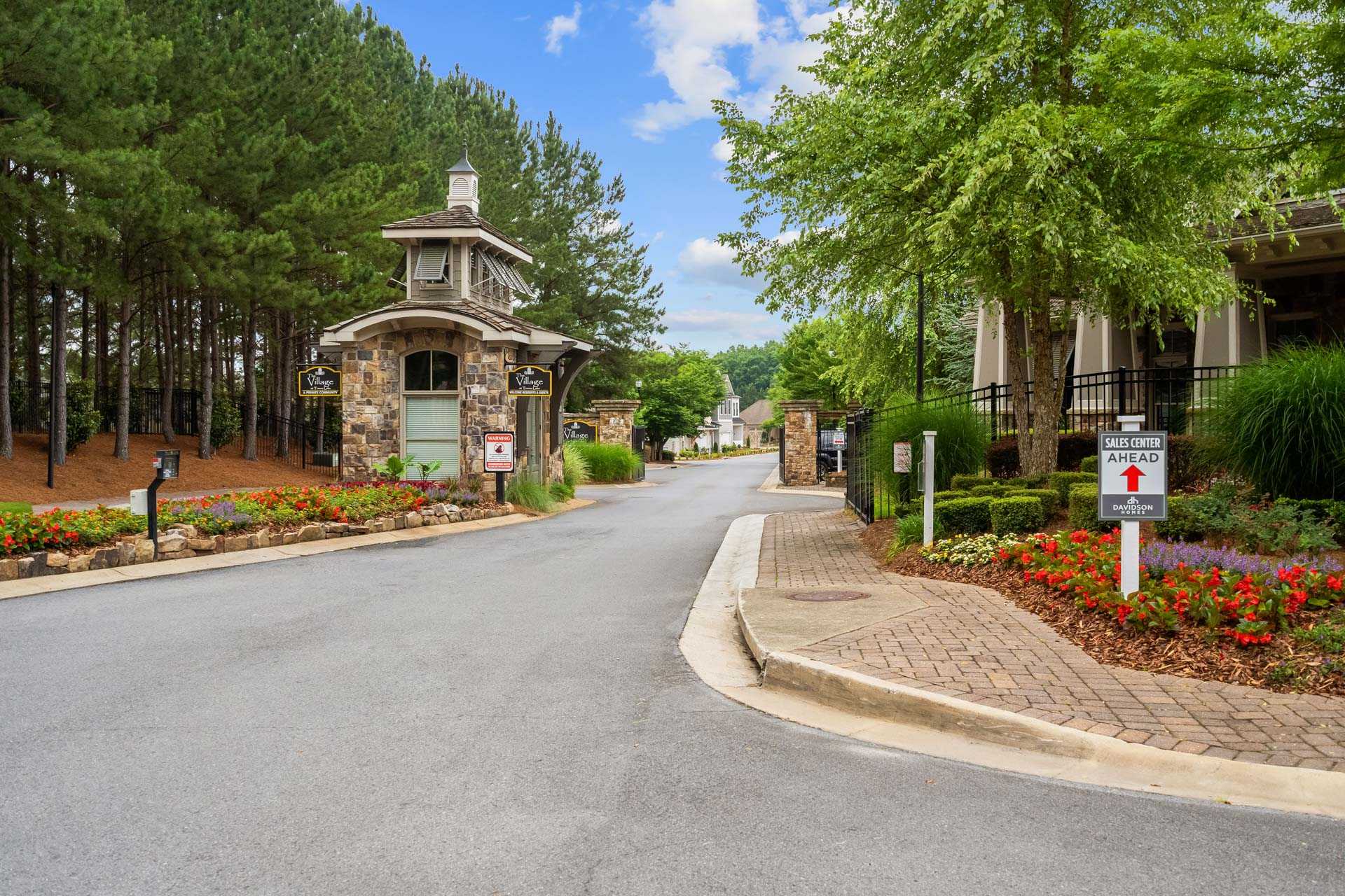 Elegant stone and wood gated entrance at The Village at Towne Lake in Woodstock Georgia surrounded by pine trees and colorful flower beds