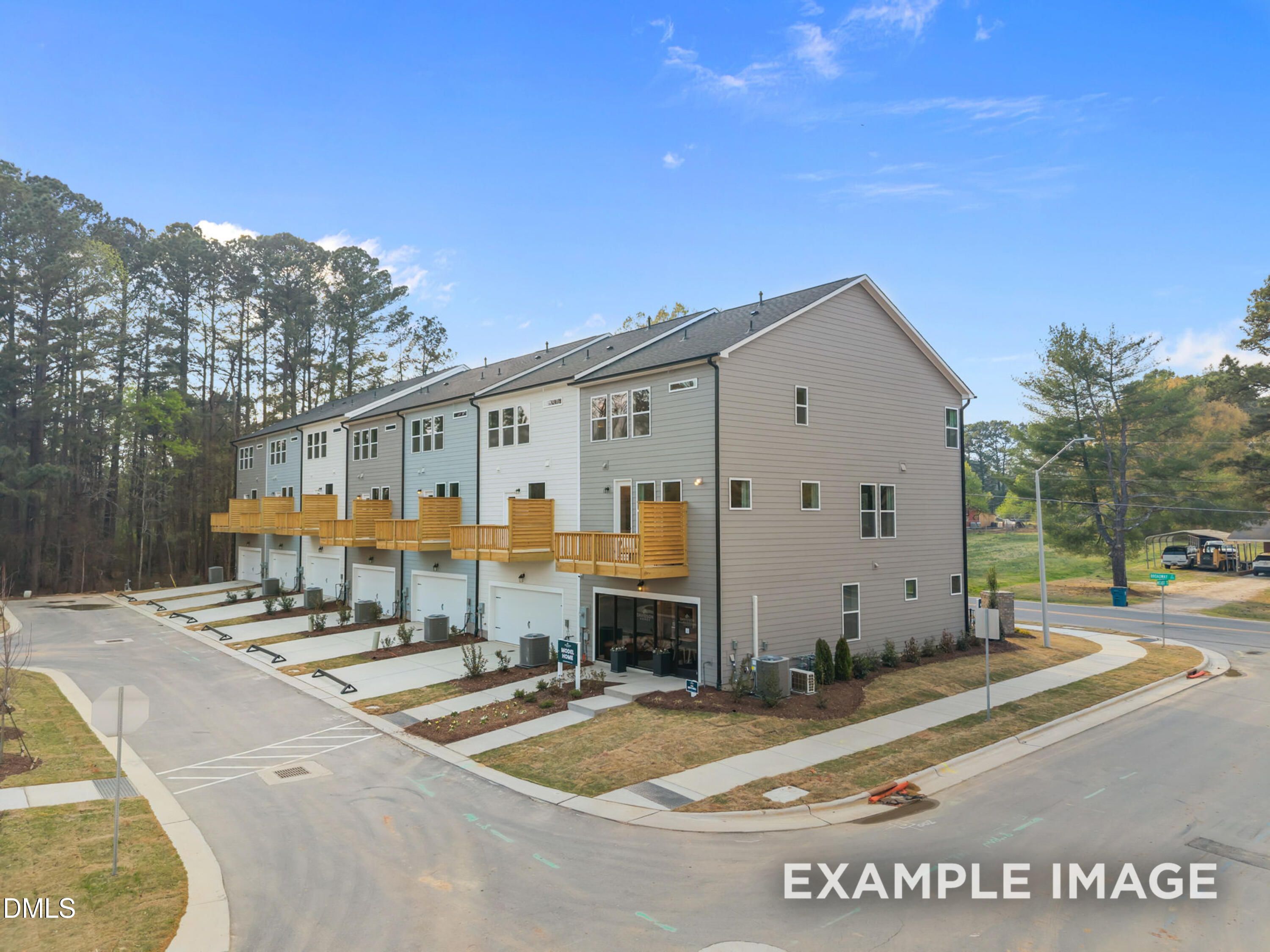 Row of modern 3-story townhomes with garages, wooden balconies, and pine surroundings in Camden Park, Knightdale, NC by Davidson Homes