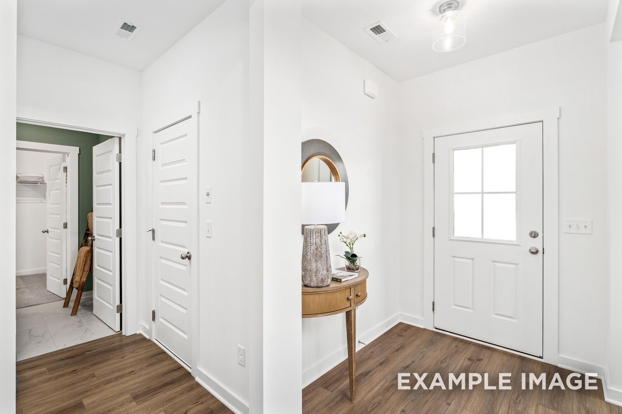 Bright entry foyer with wood floors, round mirror, console table lamp, and white front door in Davidson Homes The Ash A, Gallatin, TN