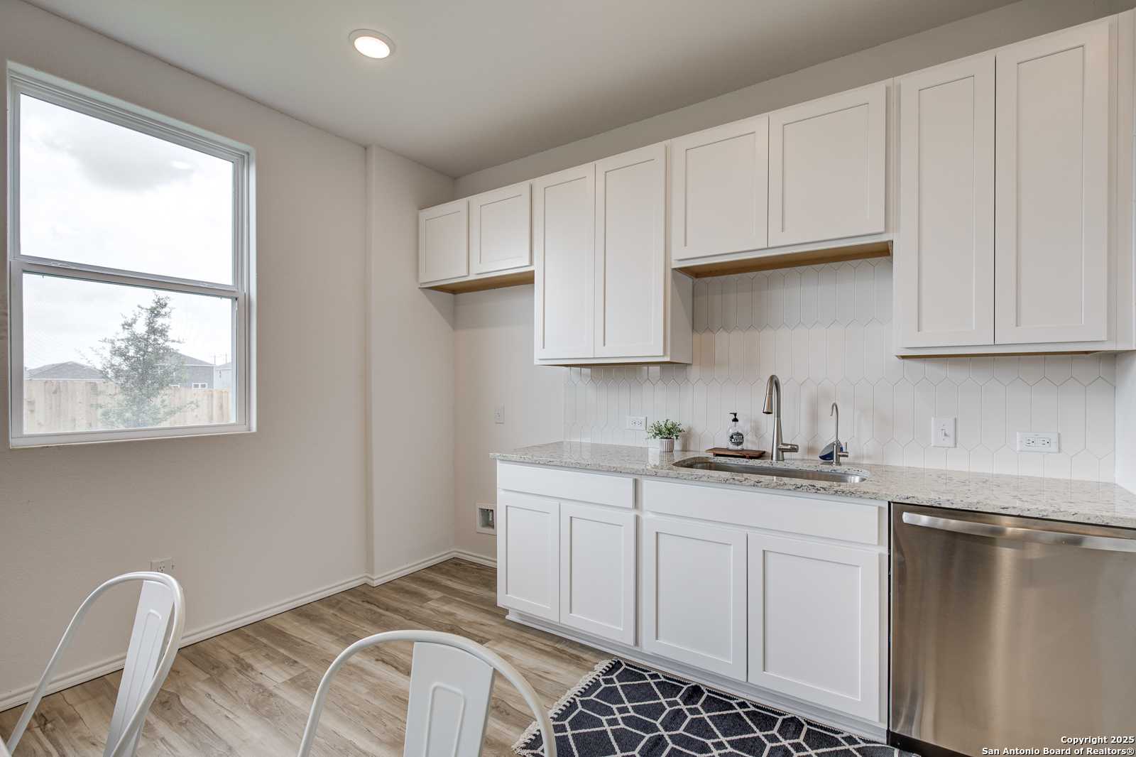Modern white kitchen with shaker cabinets, stainless dishwasher, quartz counters and large window in Davidson Homes Trinity A, San Antonio
